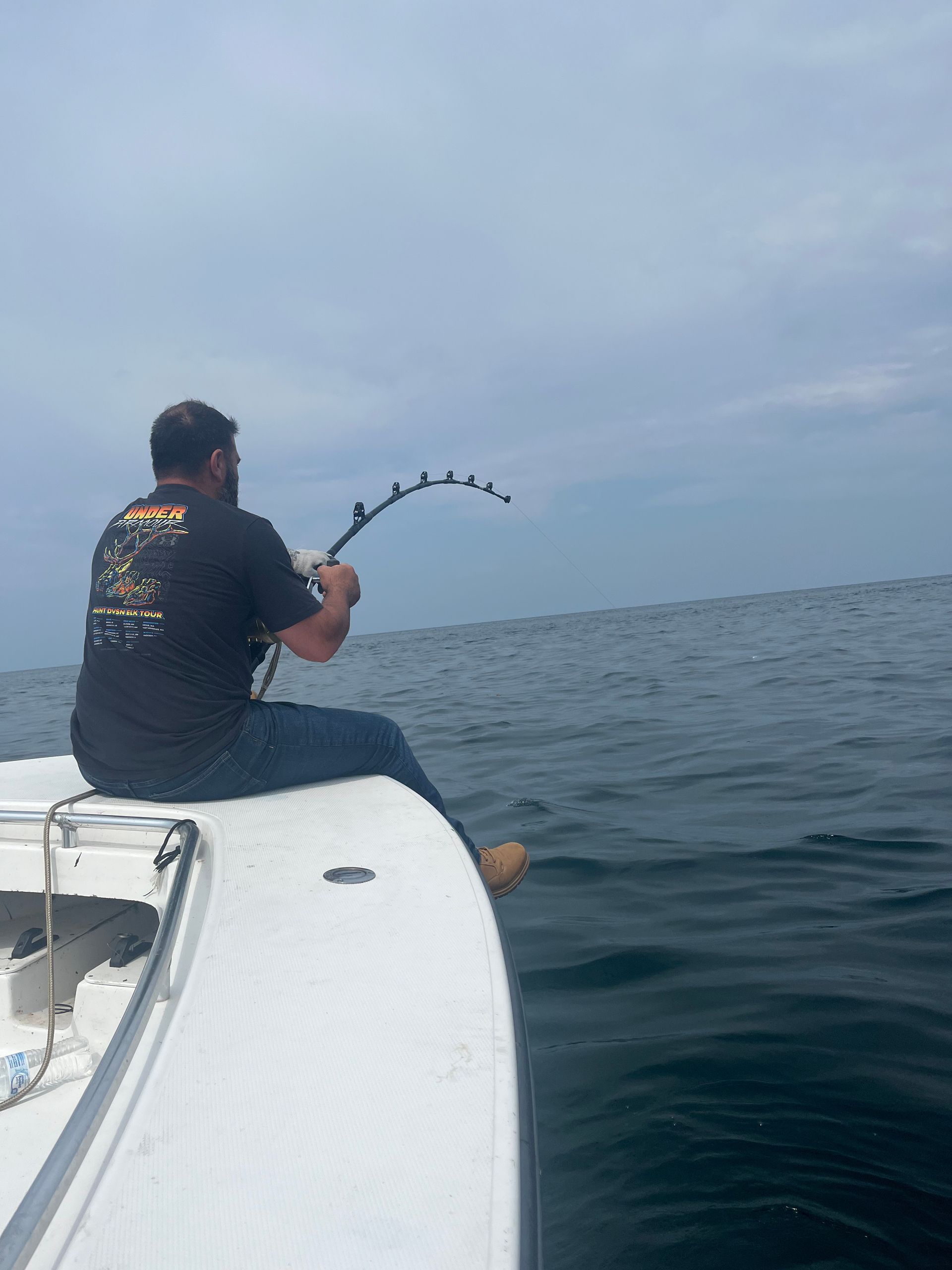 A man is sitting on the back of a boat fishing in the ocean.