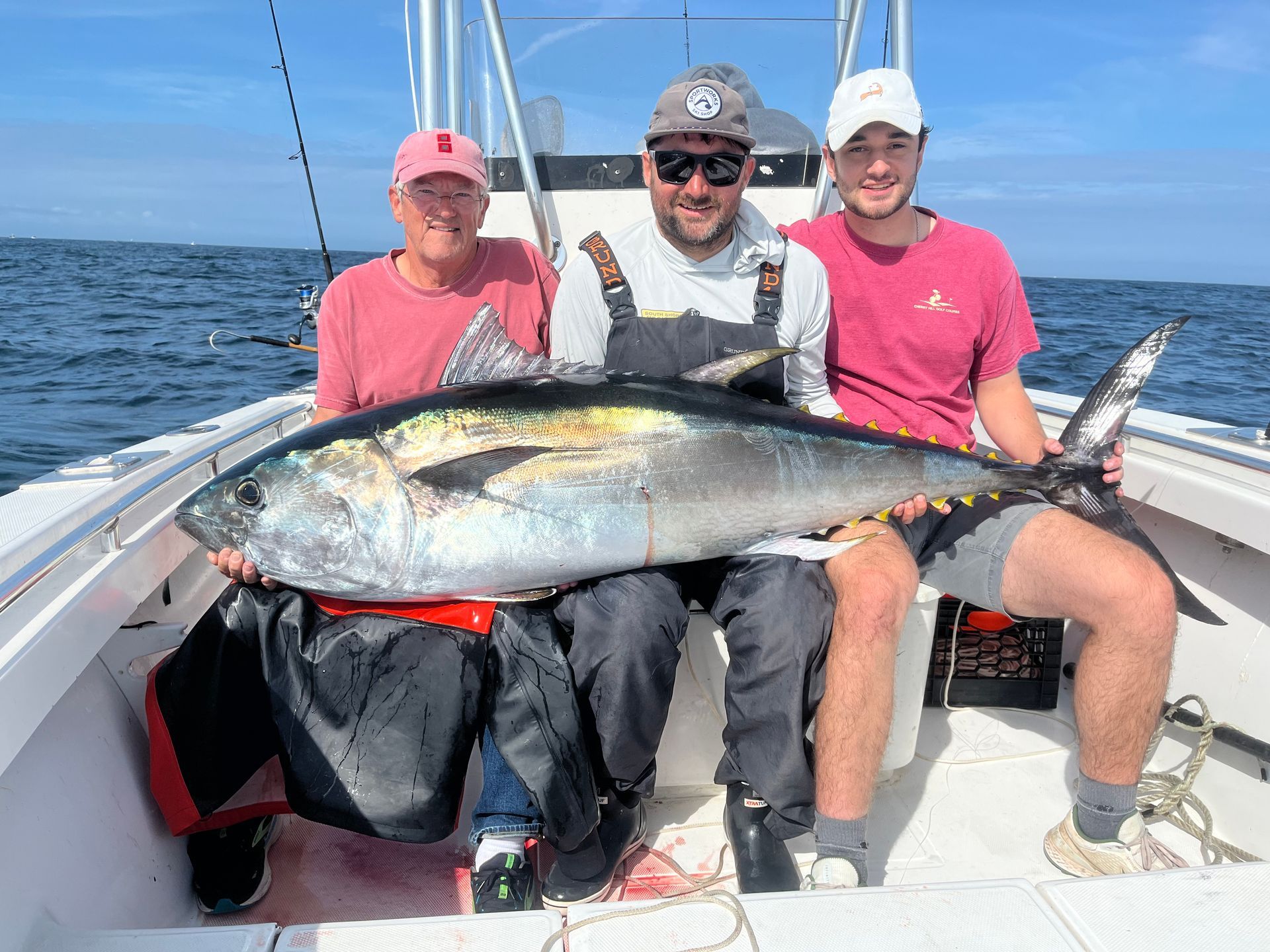 Three men are sitting on a boat holding a large fish.