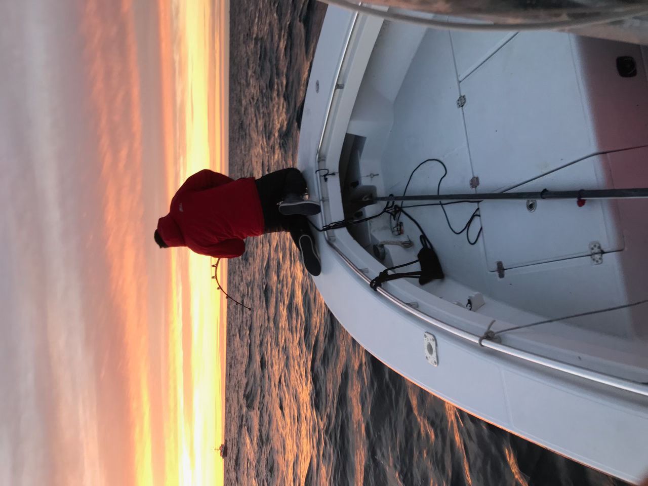 A person in a red jacket is standing on a boat in the water