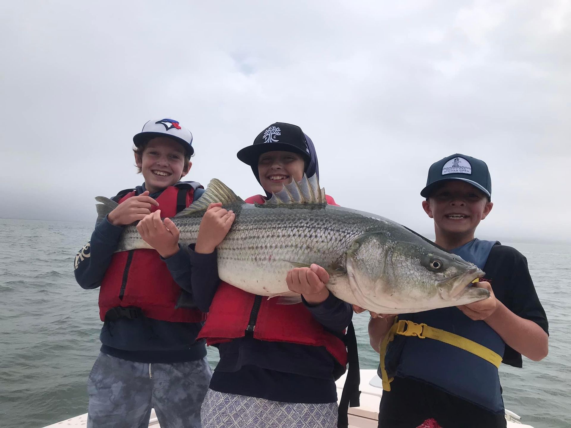 Three children are holding a large fish on a boat.