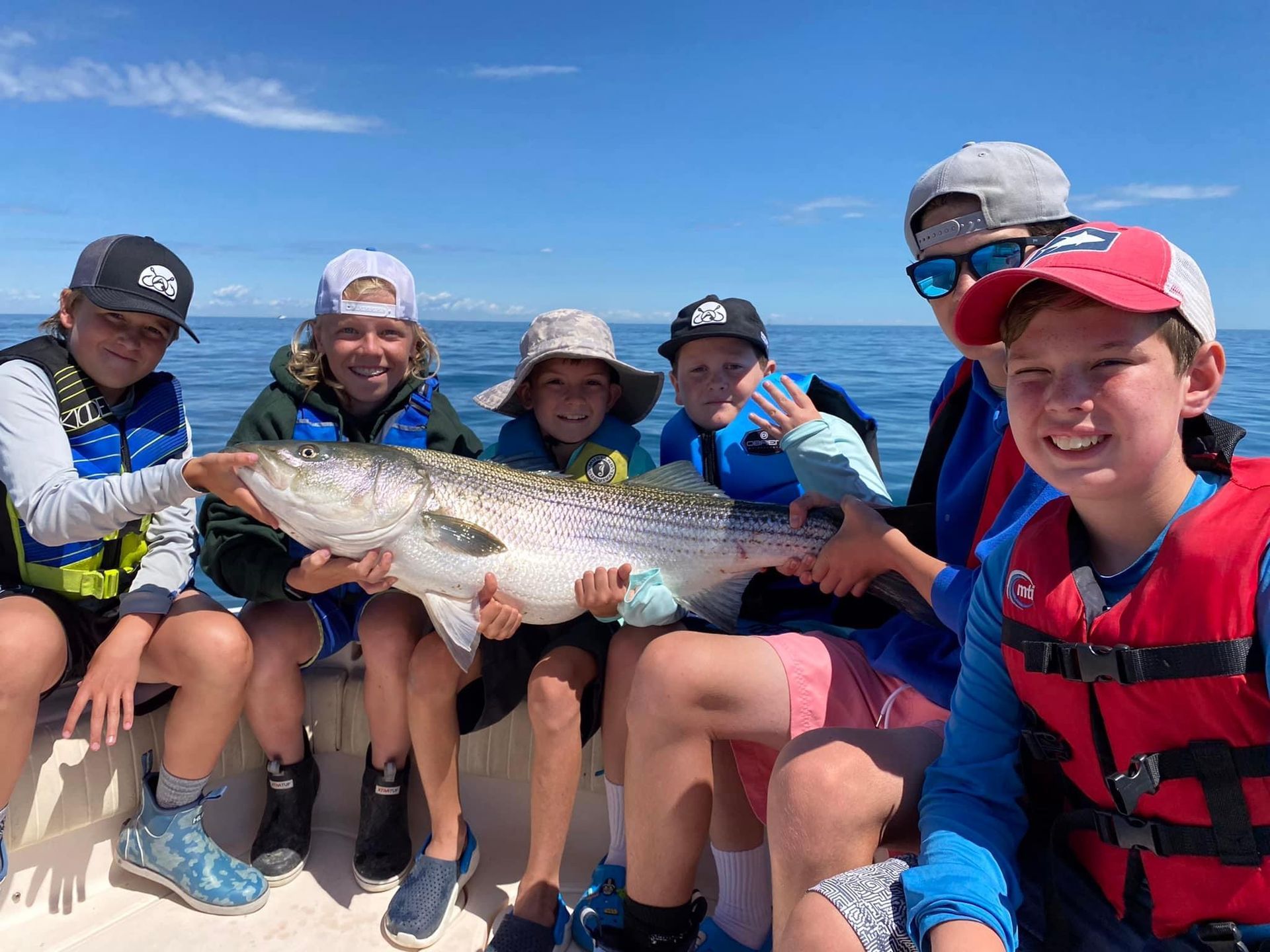 A group of children are sitting on a boat holding a large fish.