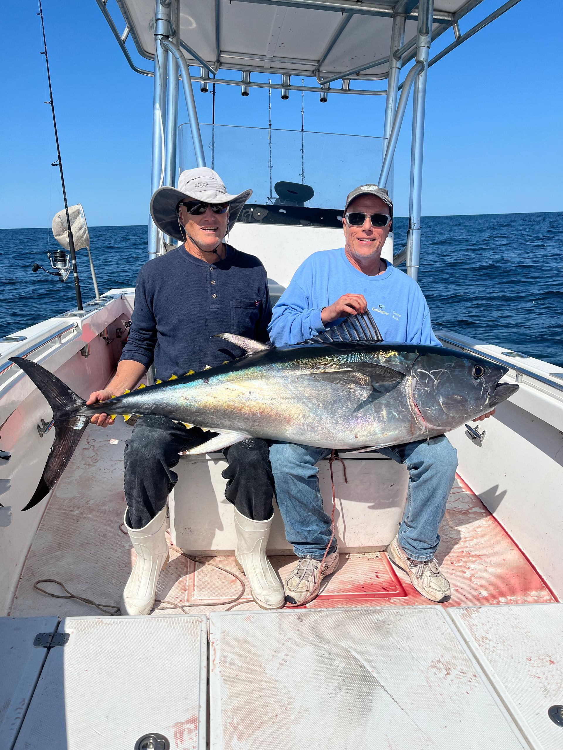 Two men are sitting on a boat holding a large fish.