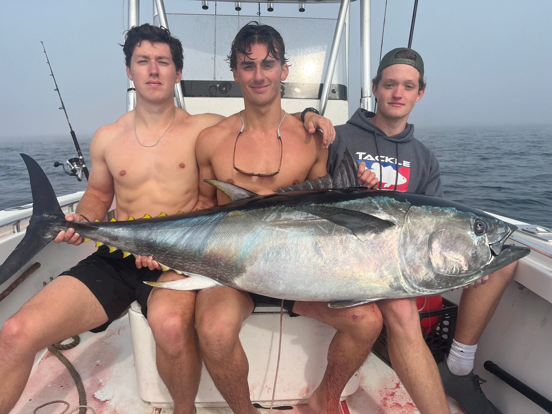 Three men are sitting on a boat holding a large fish