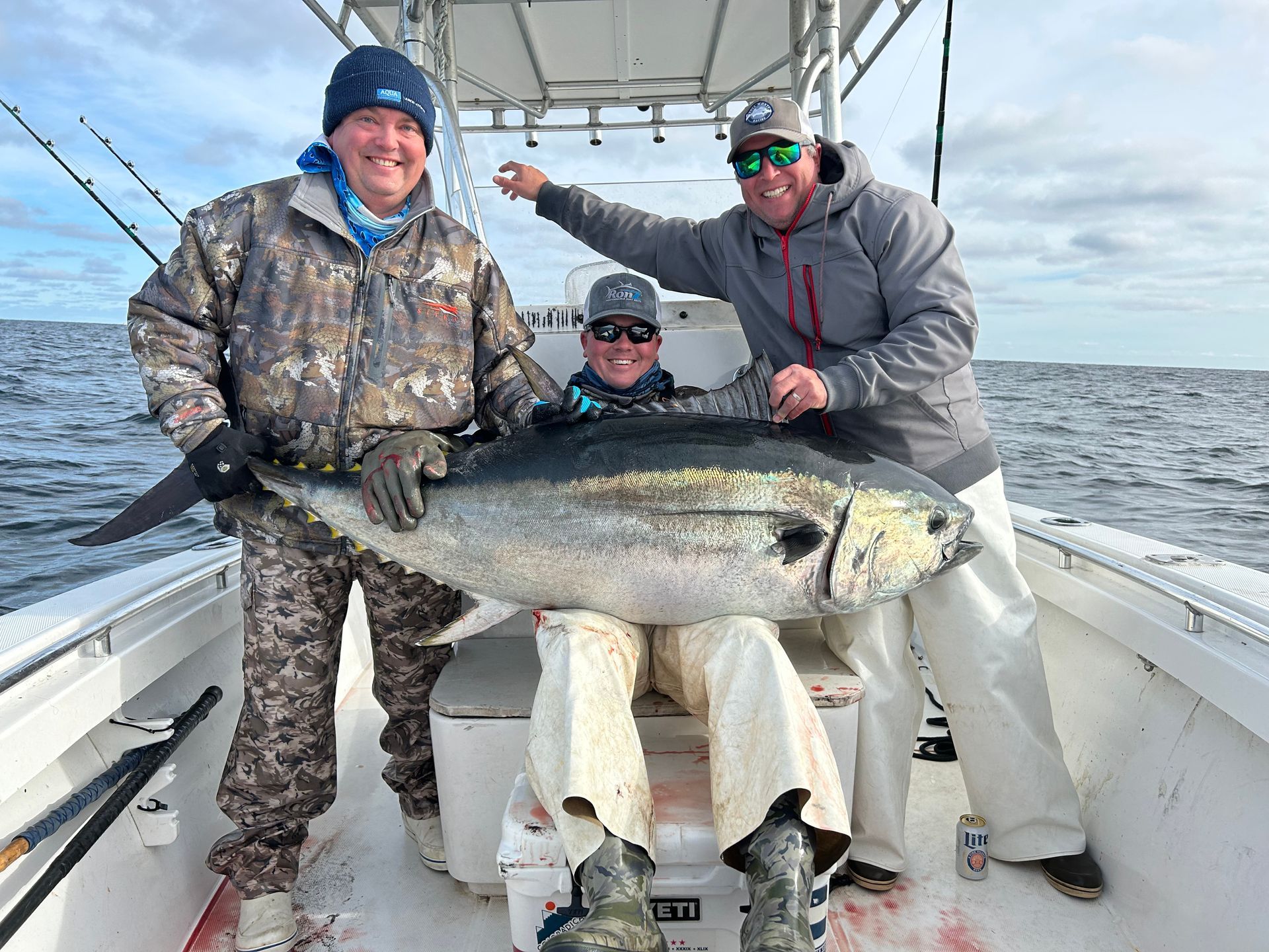 Three men are standing on a boat holding a large fish.