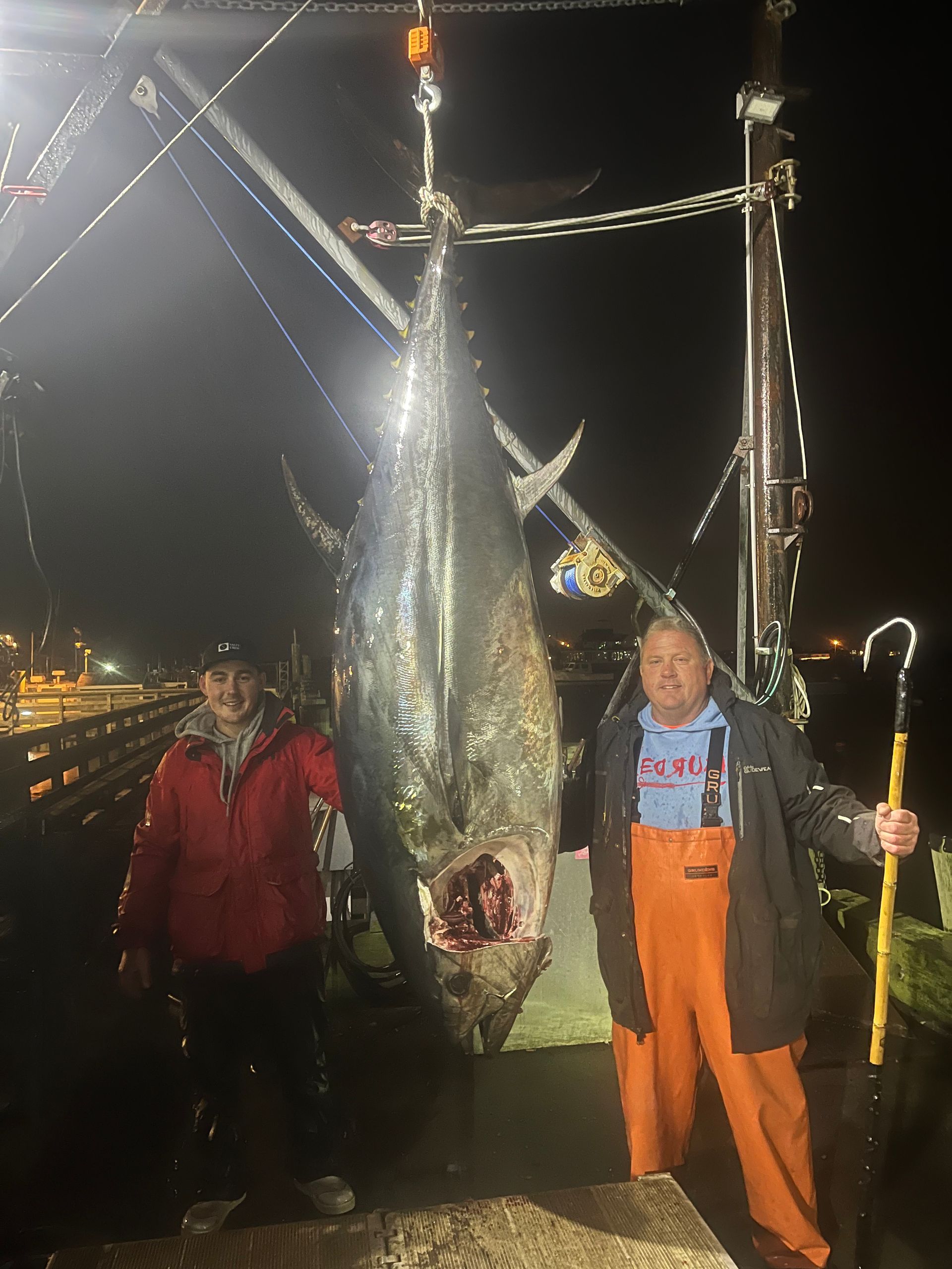 Two men are standing next to a large fish on a dock.