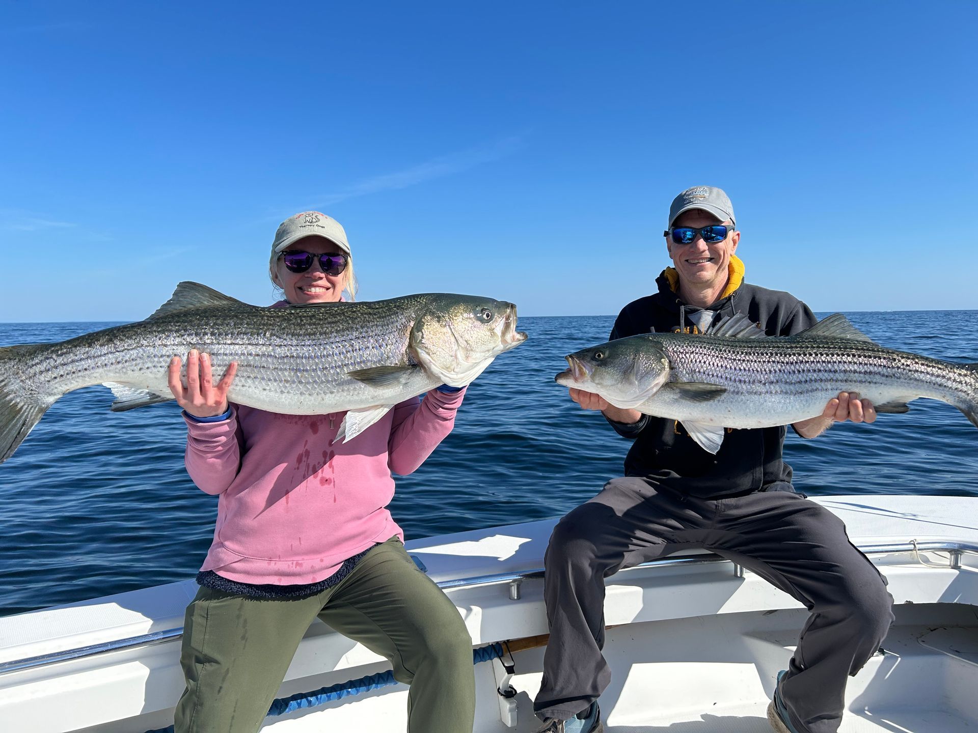 A man and a woman are sitting on a boat holding large fish.