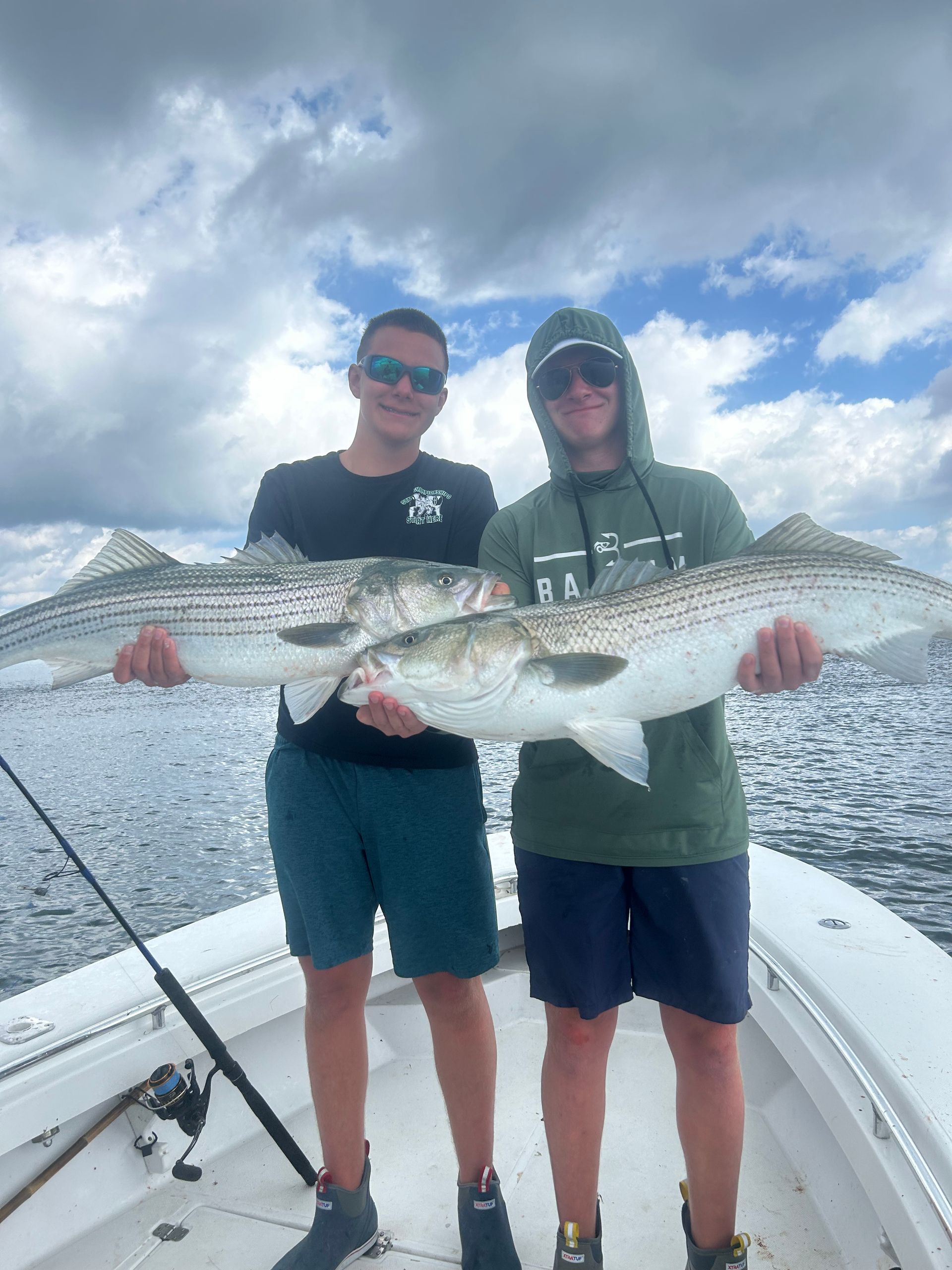 Two men are standing on a boat holding a large fish.