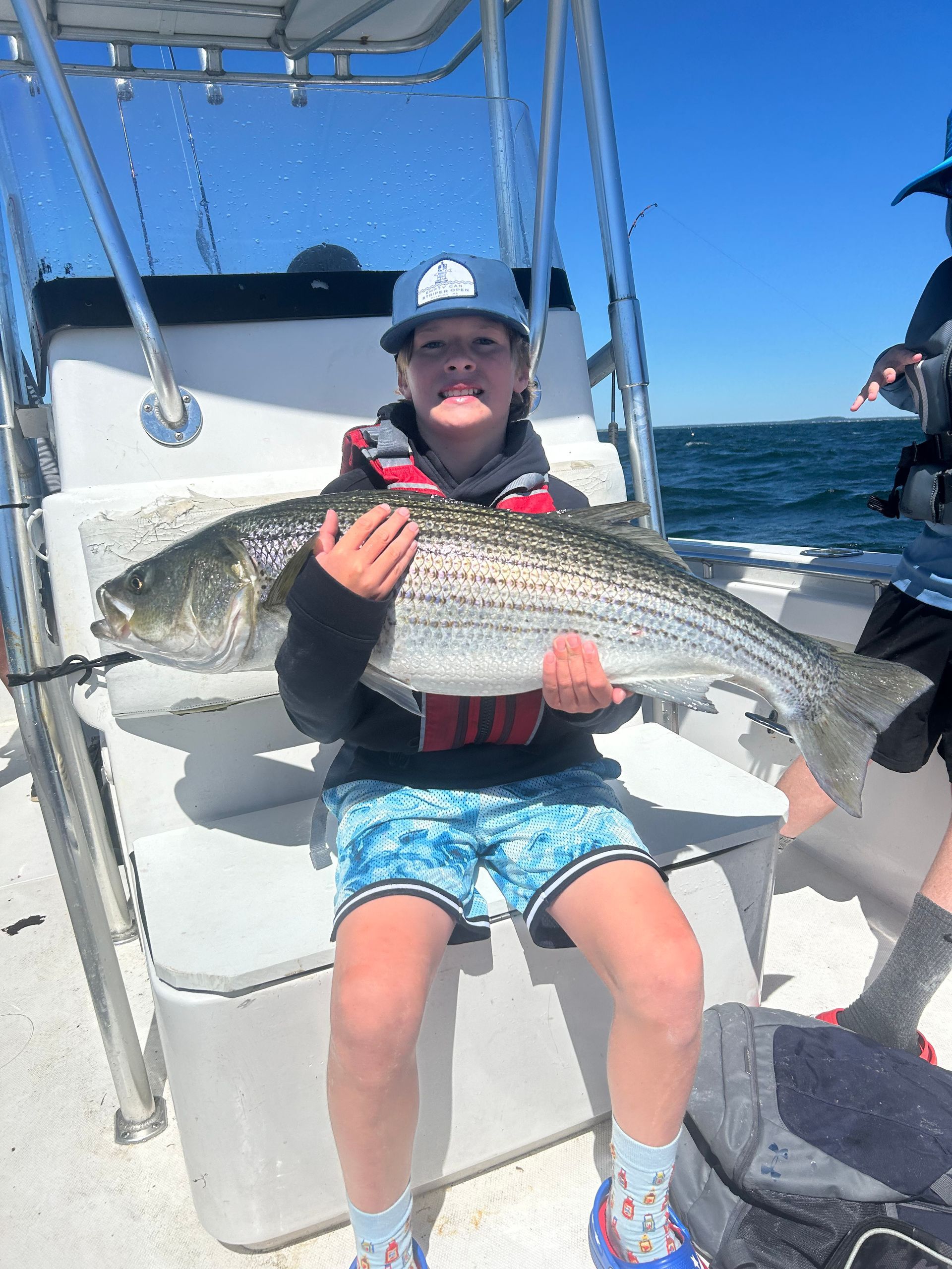 A young boy is sitting on a boat holding a large fish.