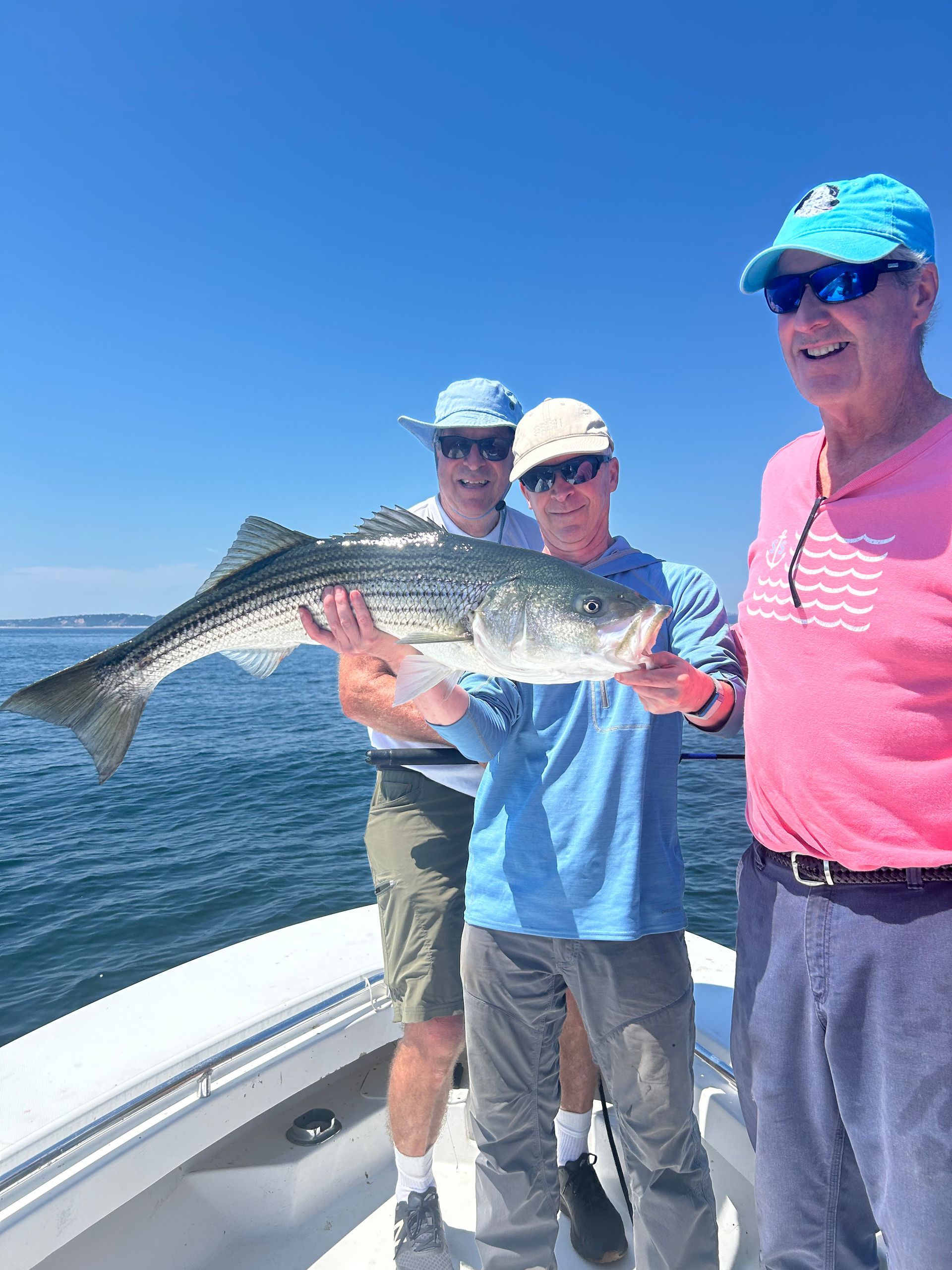 Three men are standing on a boat holding a large fish.