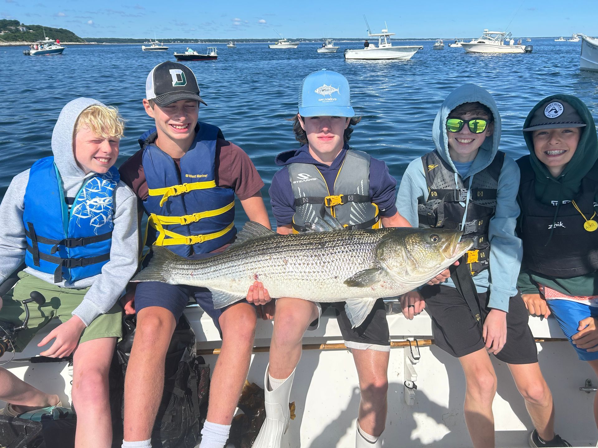A group of young people are sitting on a boat holding a large fish.