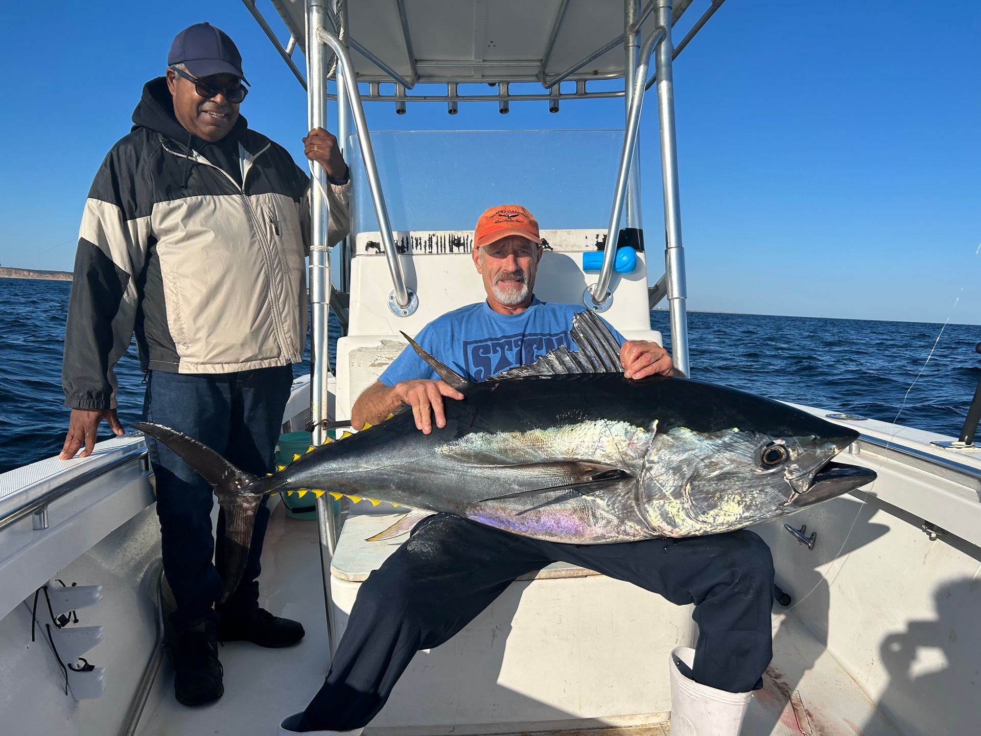 Two men are sitting on a boat holding a large fish.