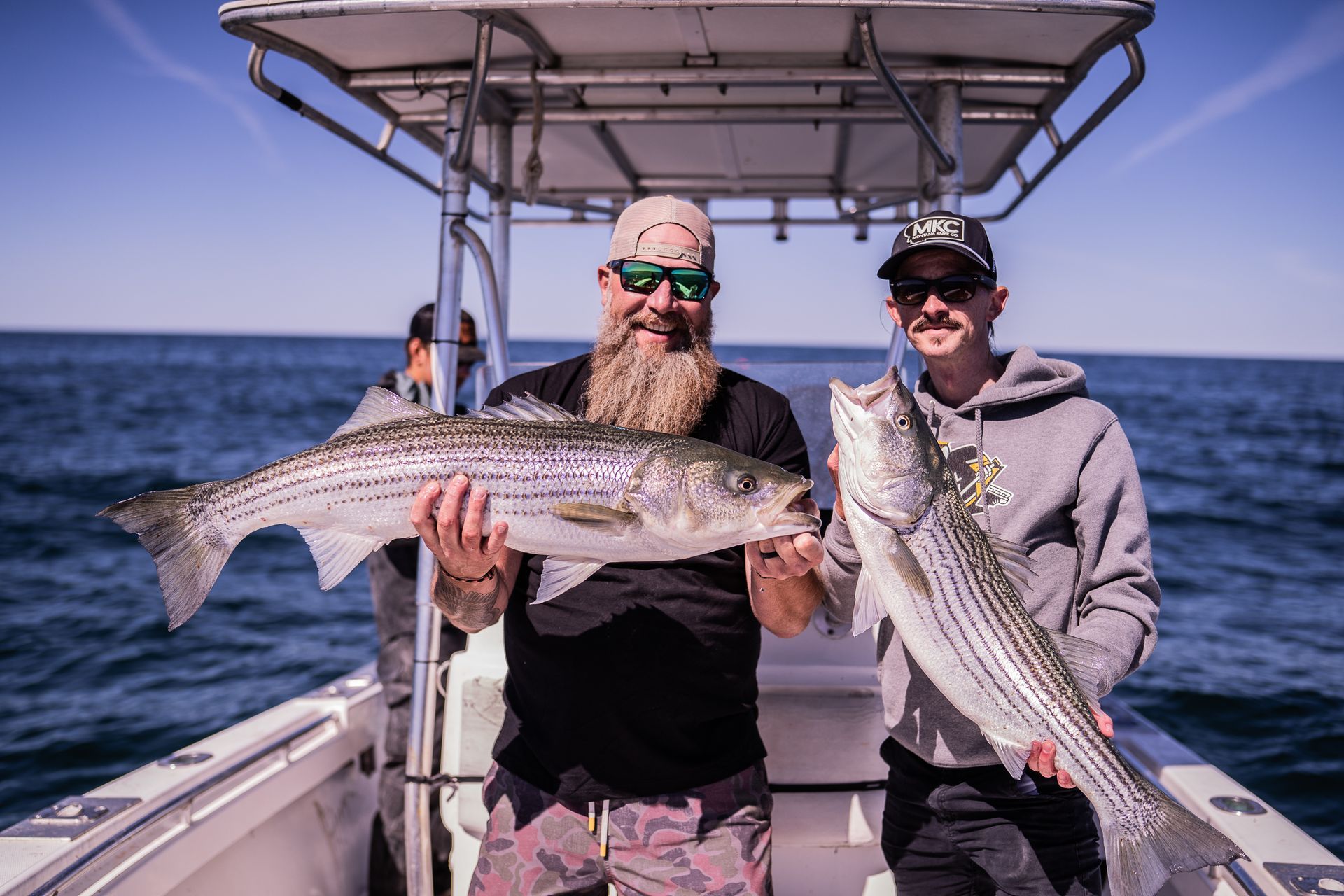 Two men are holding large fish on a boat in the ocean.
