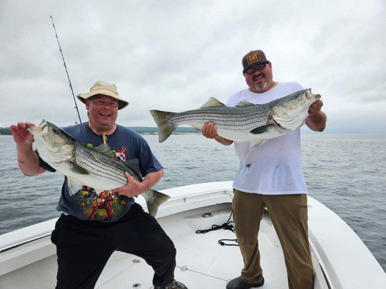 Two men are standing on a boat holding large fish.