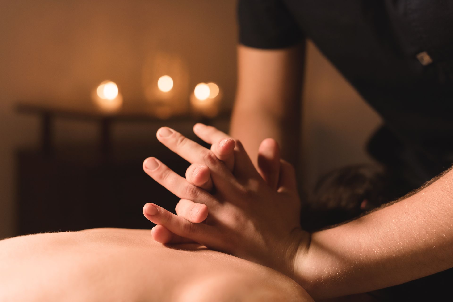 Massage therapist kneading a person's back in a dimly lit spa with candles in the background