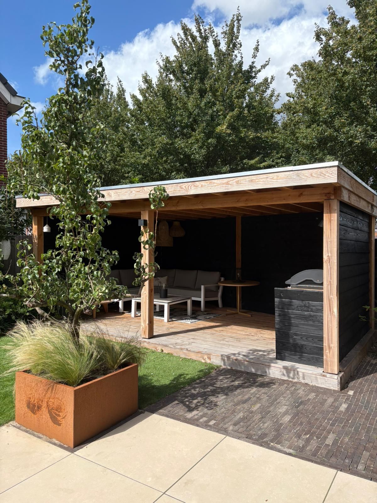 Houten tuinpaviljoen met zitgelegenheid, barbecue en sierplanten.