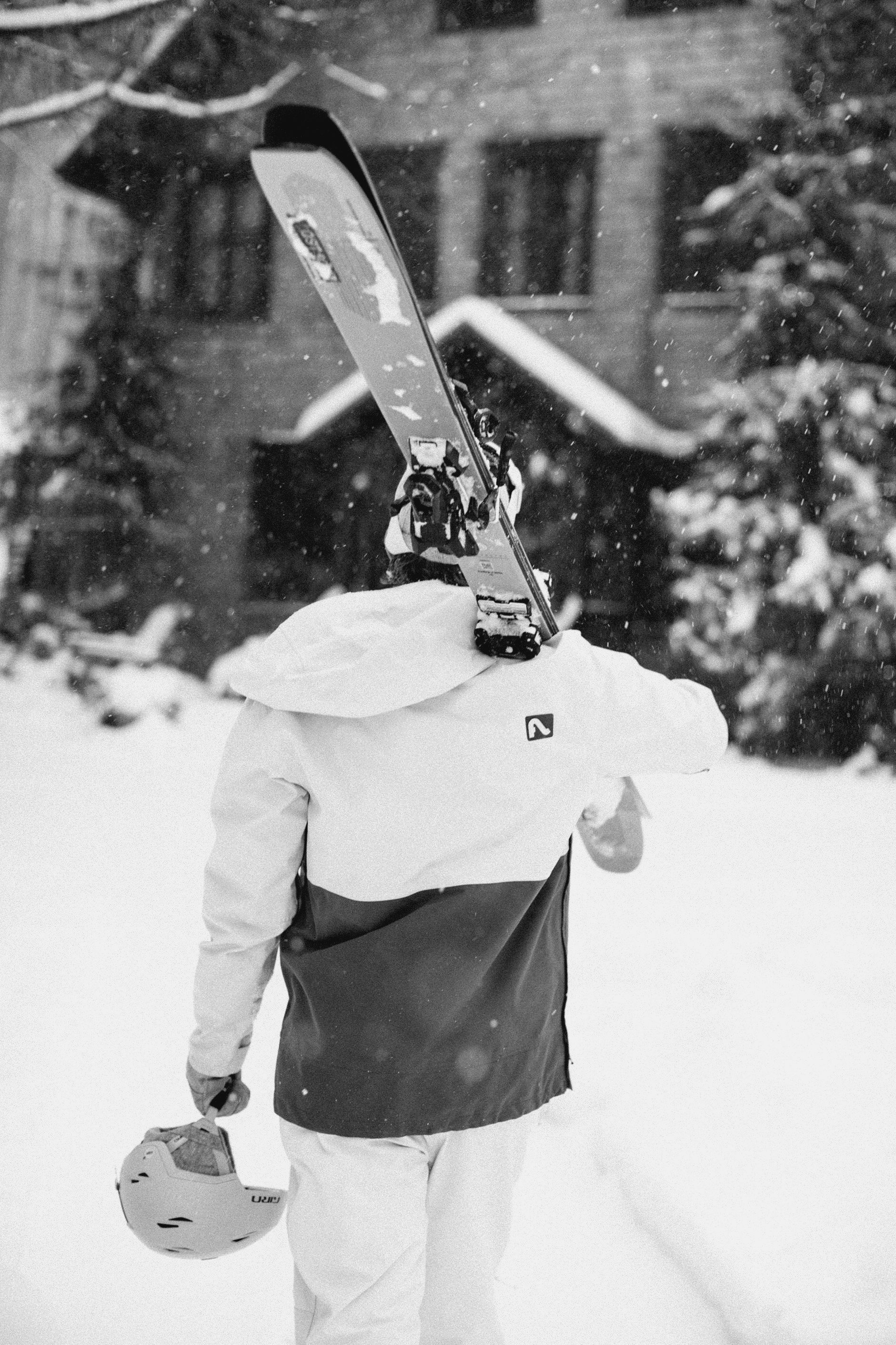 A person is carrying skis and a helmet in the snow.