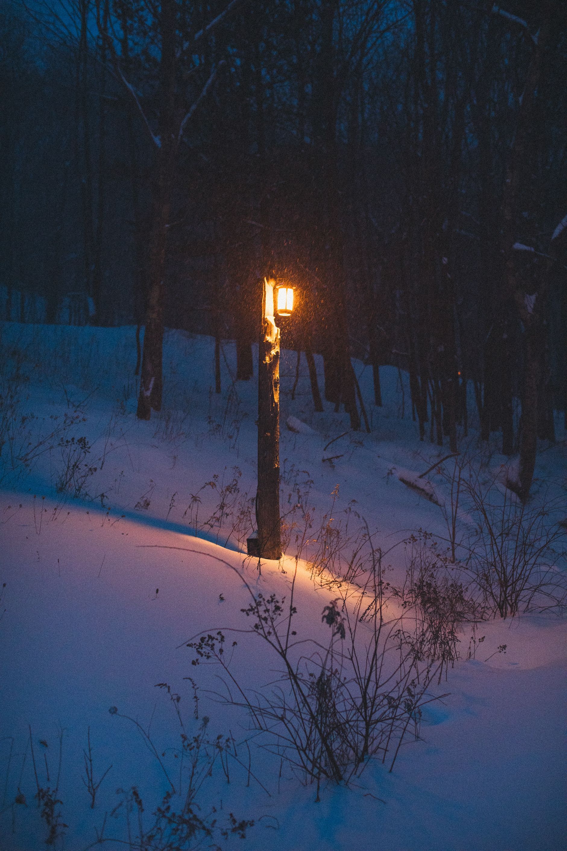 A street light is lit up in the snow at night.