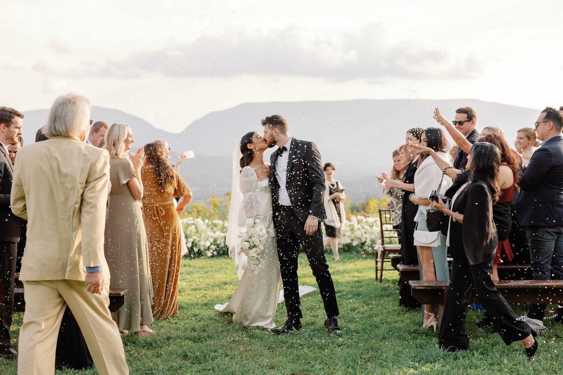 A bride and groom are kissing in front of their wedding guests.