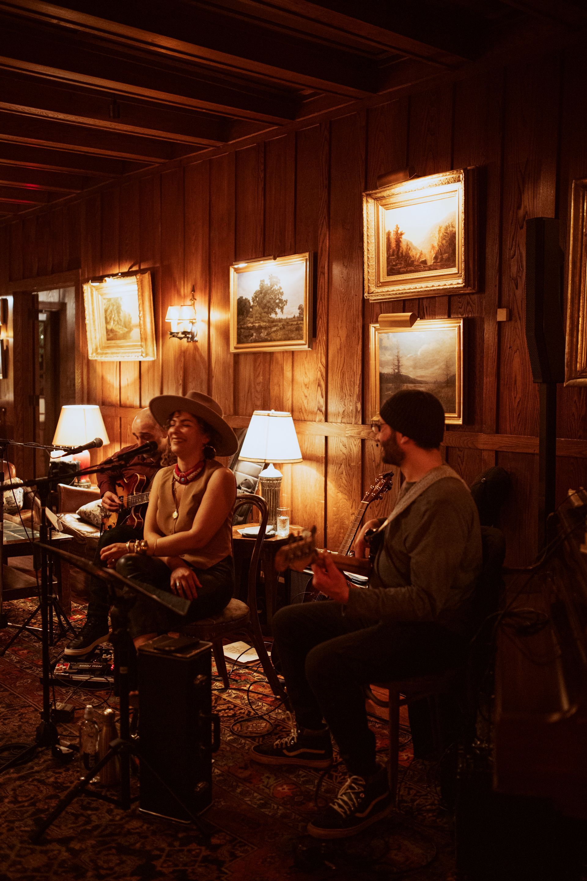 A man and a woman are playing instruments in a room with wood paneling.