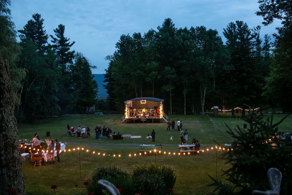 A group of people are gathered in a field with a stage in the background.