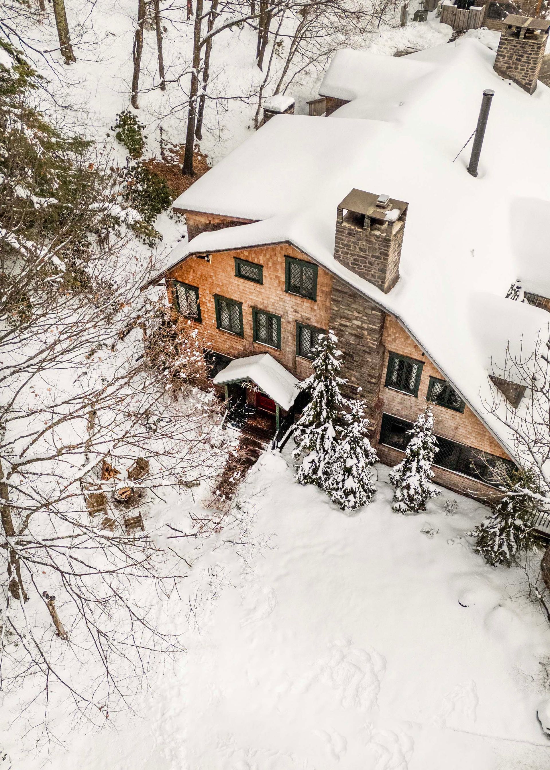 An aerial view of a house covered in snow in the woods.