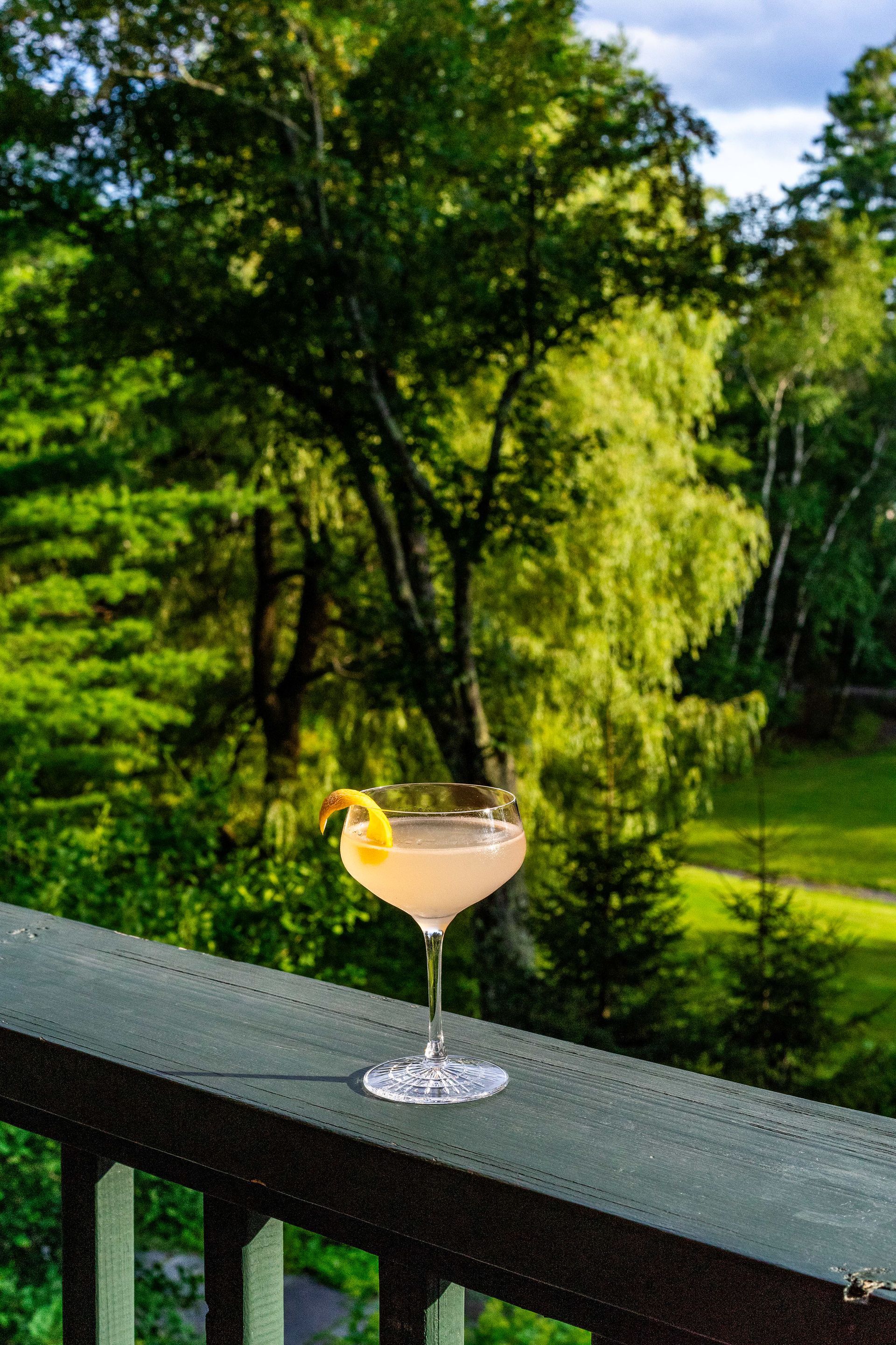 A cocktail is sitting on a balcony with trees in the background.
