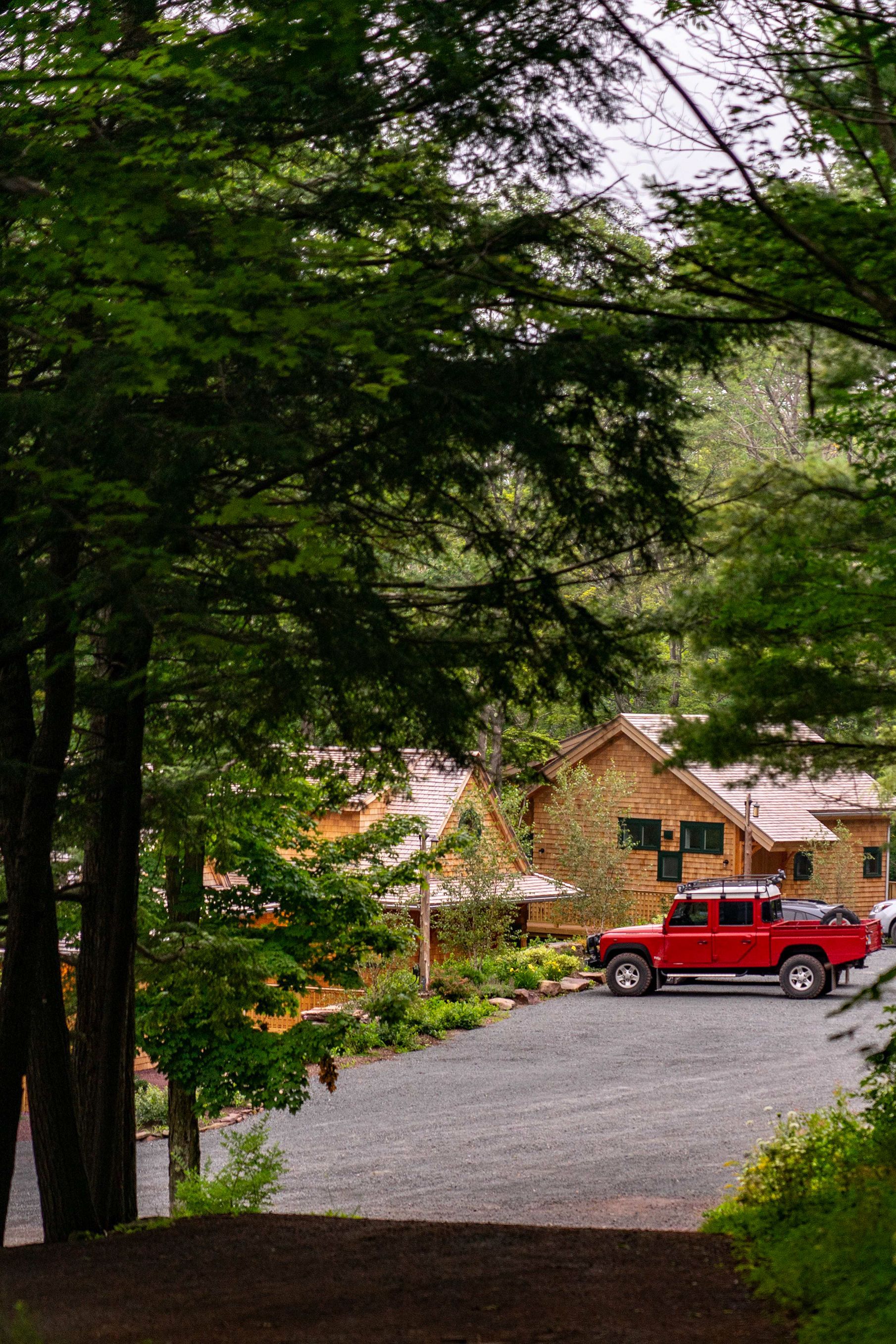 A red truck is parked in front of a cabin in the woods
