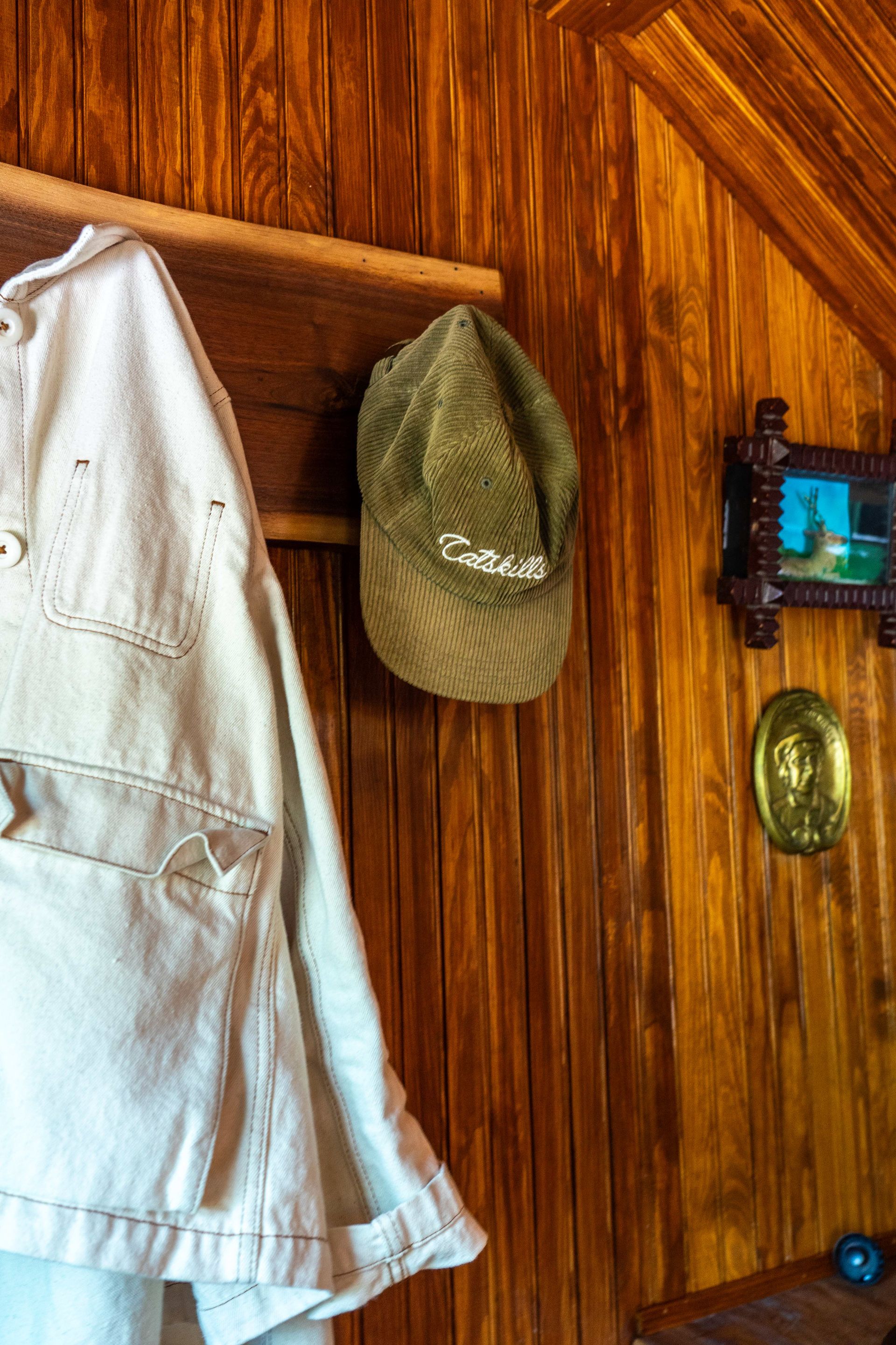 A hat is hanging on a wooden wall next to a jacket.