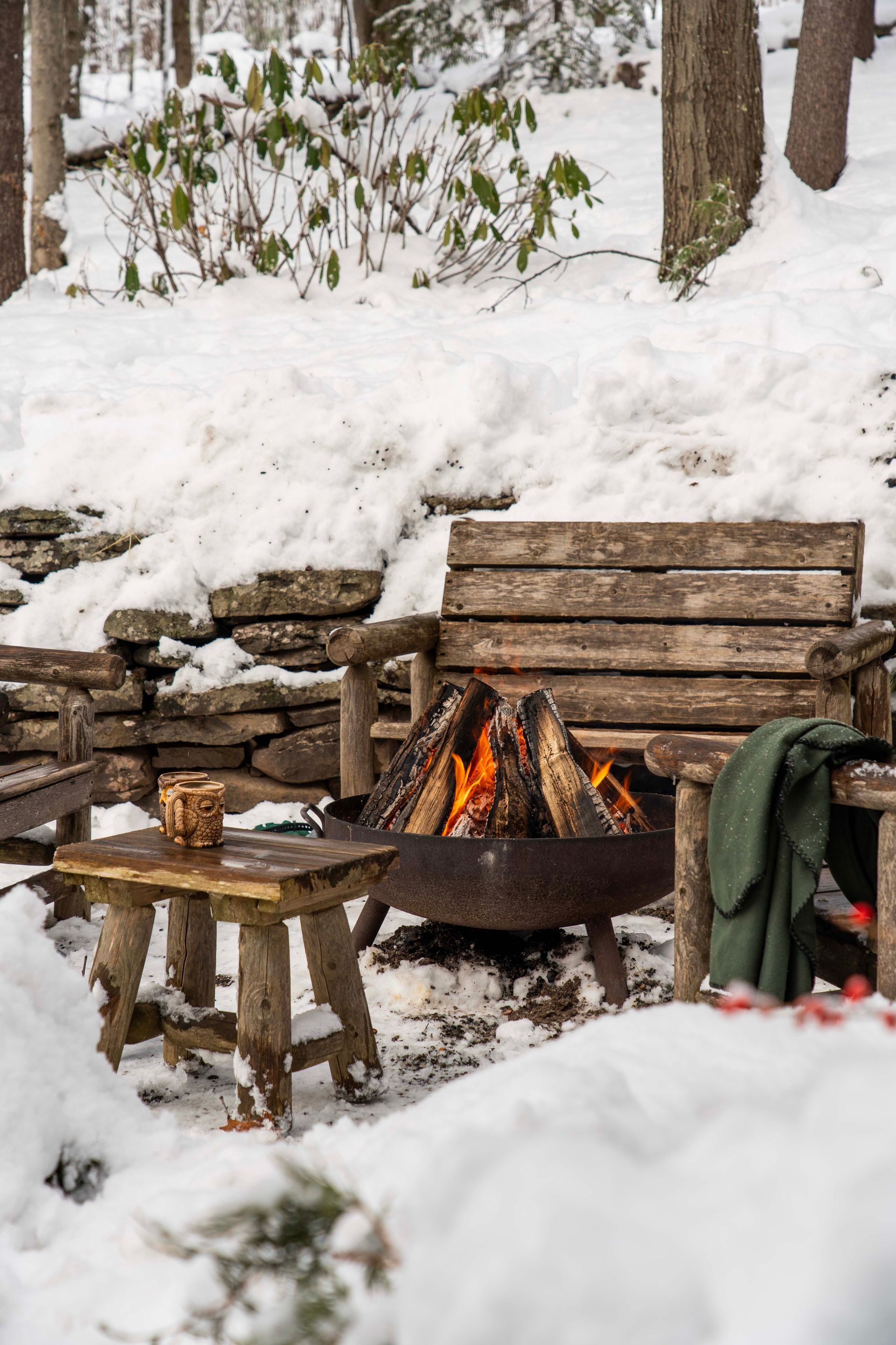 A wooden bench is sitting next to a fire pit in the snow.