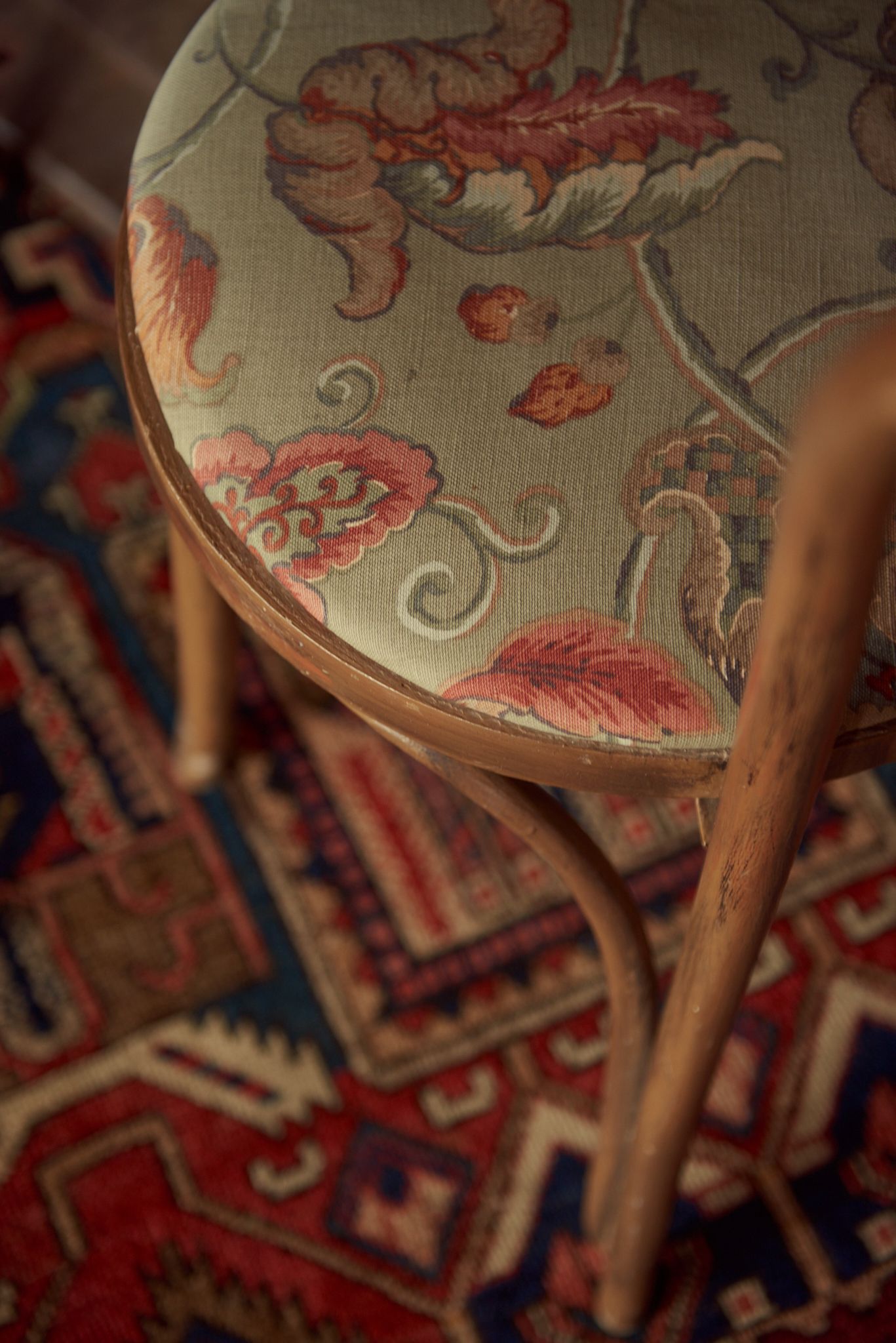 A chair with a floral pattern on the seat is sitting on a rug.