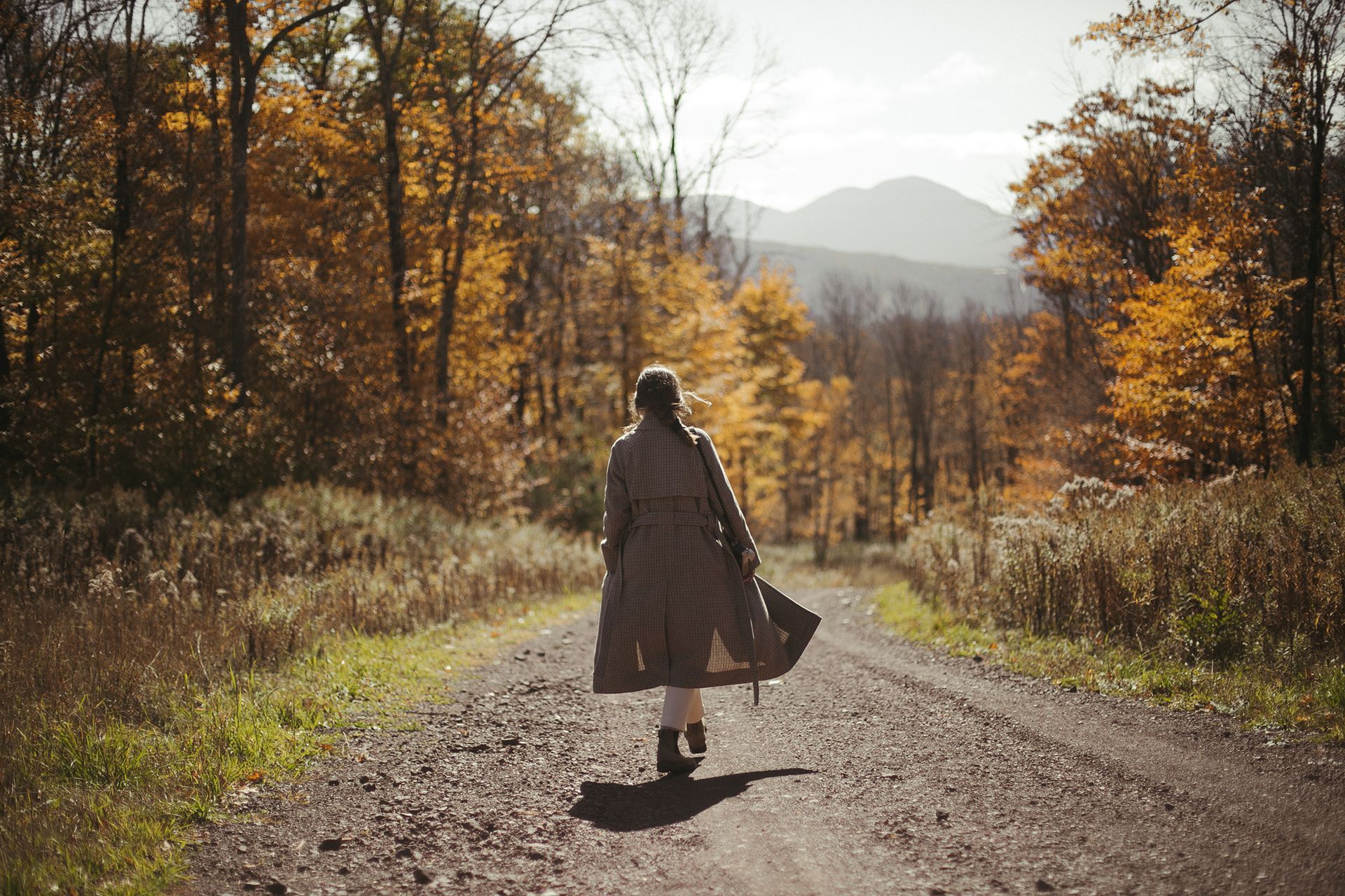 A woman is walking down a dirt road in the woods.