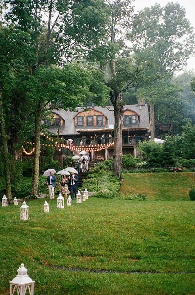 A group of people are walking in the rain in front of a large house.