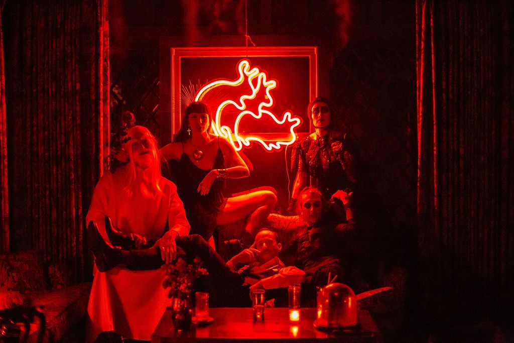 A group of people are sitting at a table in front of a neon sign.