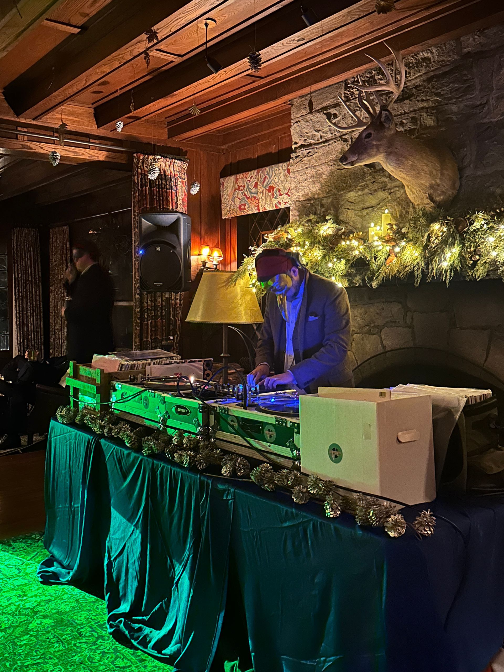 A man is playing music on a table in a room with a deer head on the wall.
