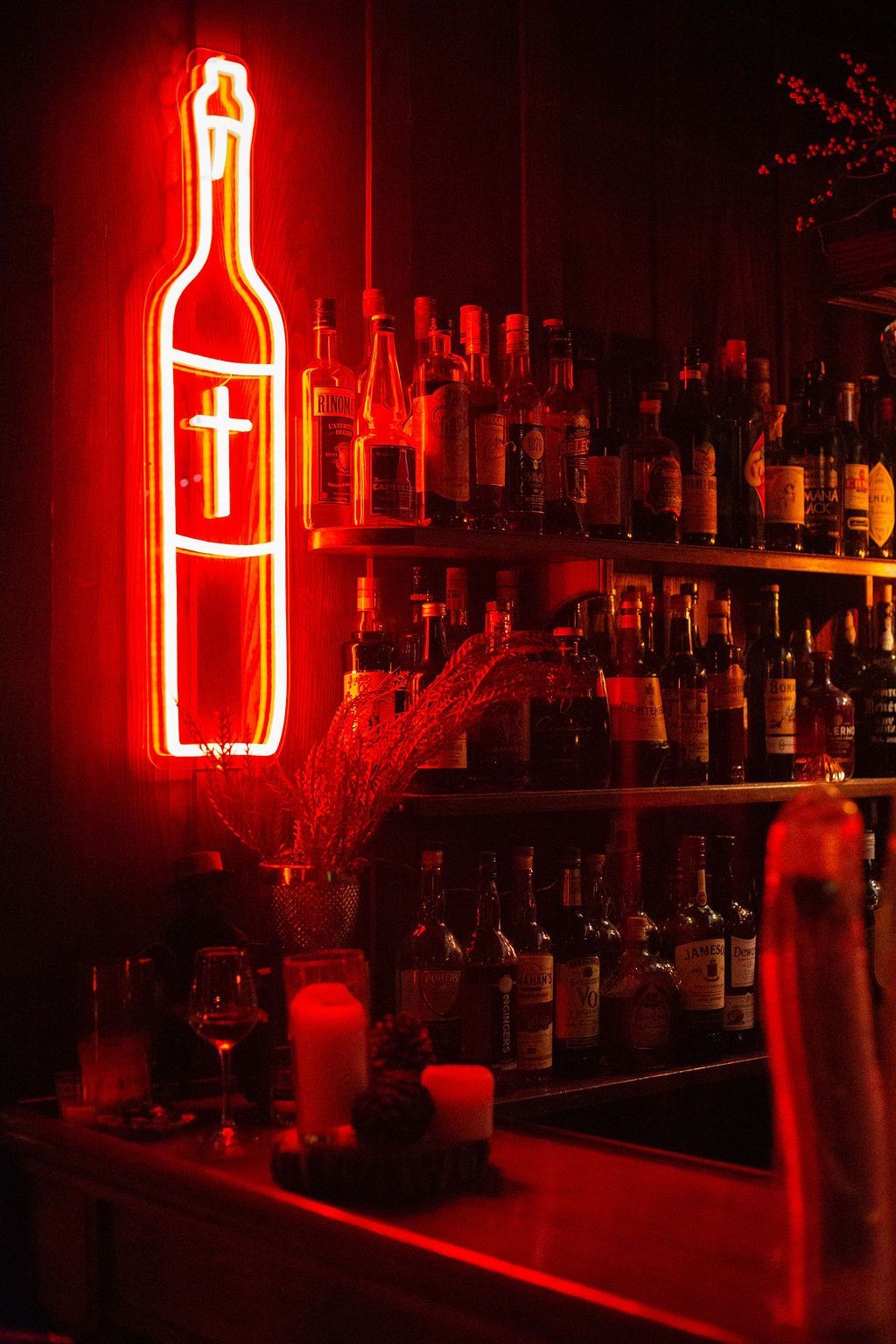 A neon sign of a bottle of wine with a cross on it is hanging from the ceiling in a bar.