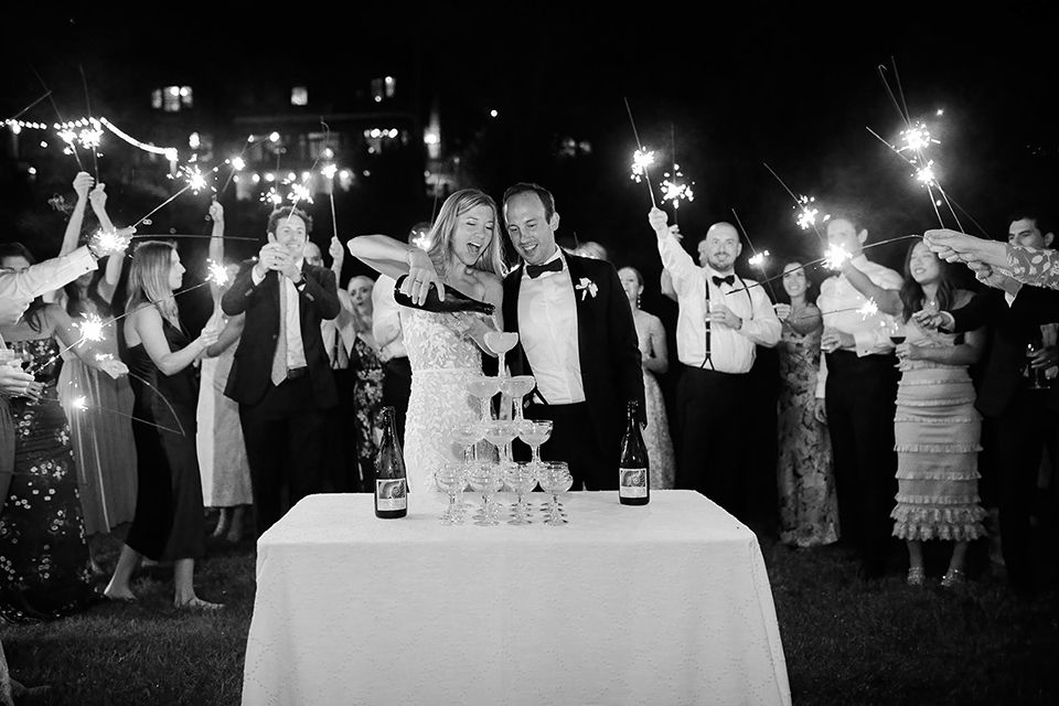 A bride and groom are cutting their wedding cake in front of a crowd of people holding sparklers.