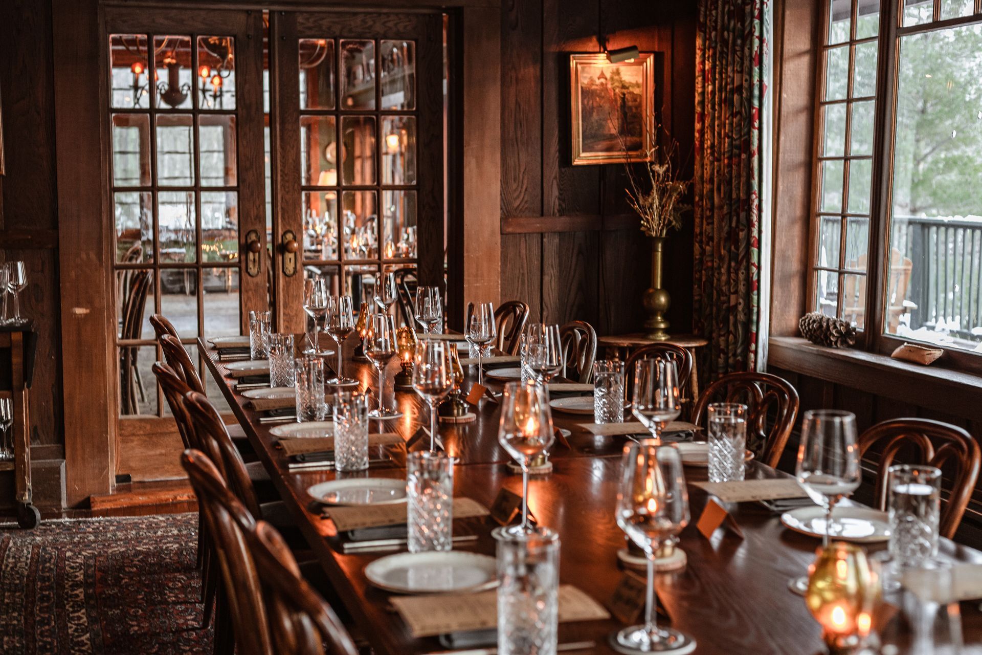 A long wooden table with plates , glasses , and candles in a restaurant.