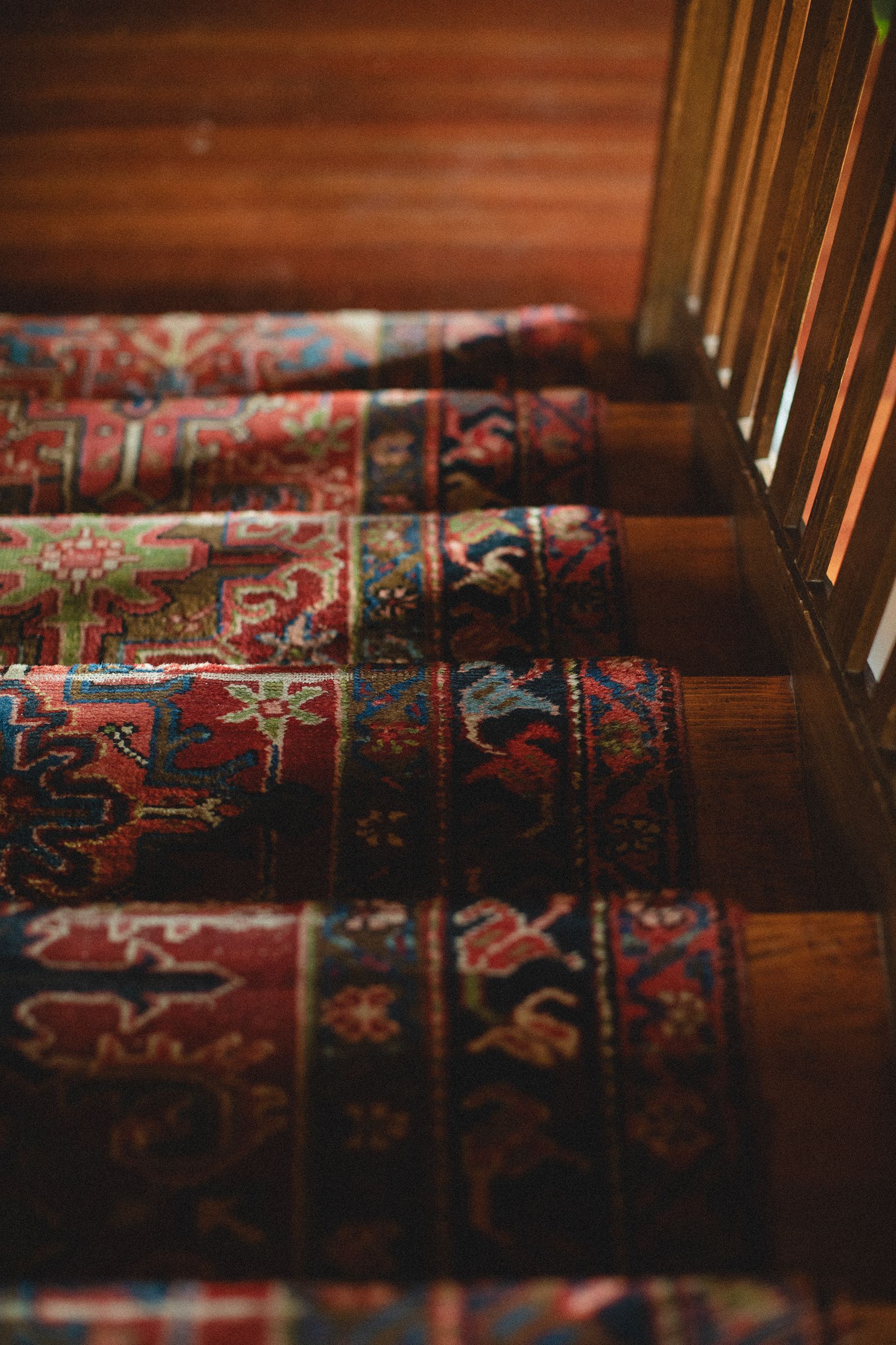 A close up of a wooden staircase with a colorful rug on the steps.