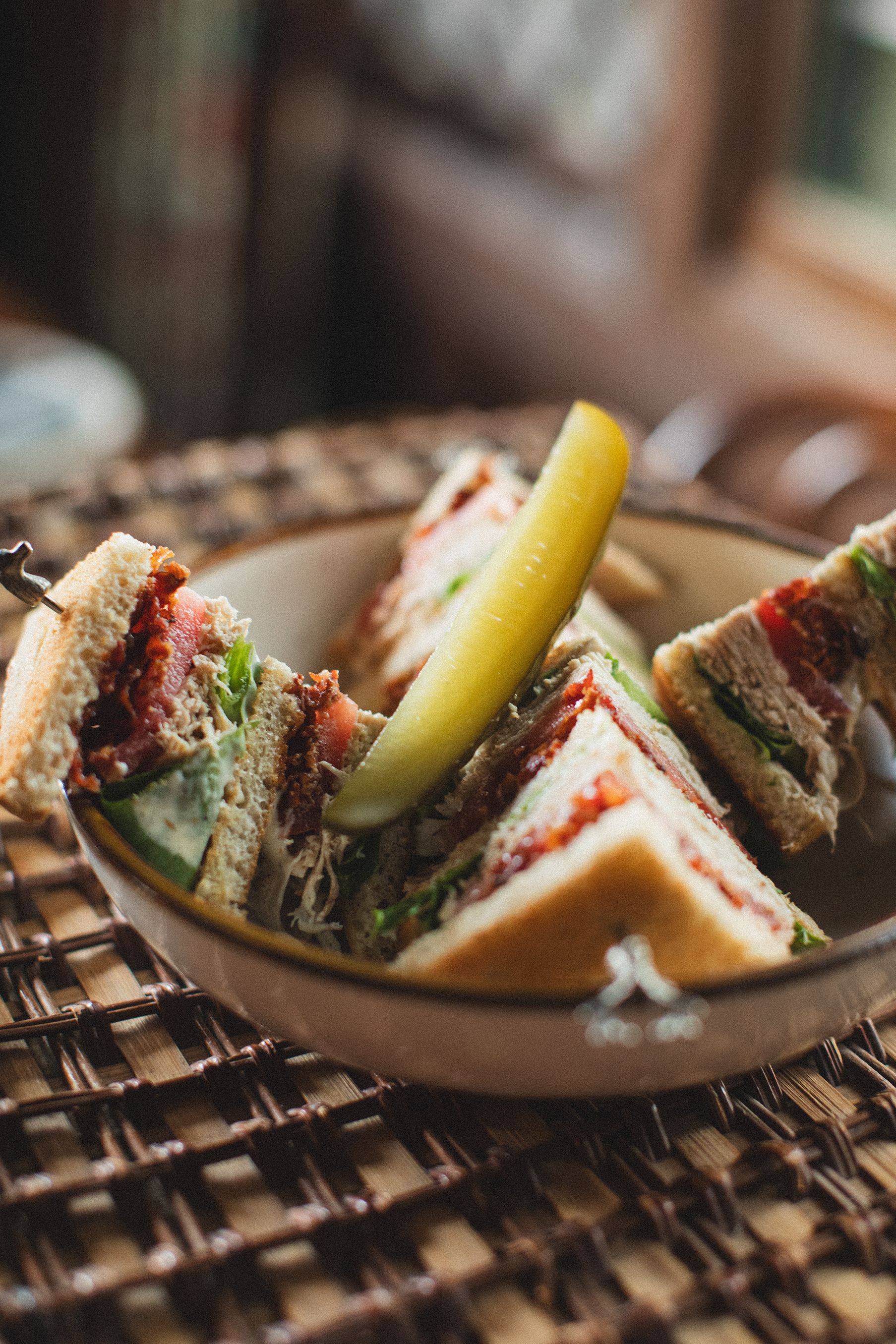 A bowl of club sandwiches with a pickle on a table.