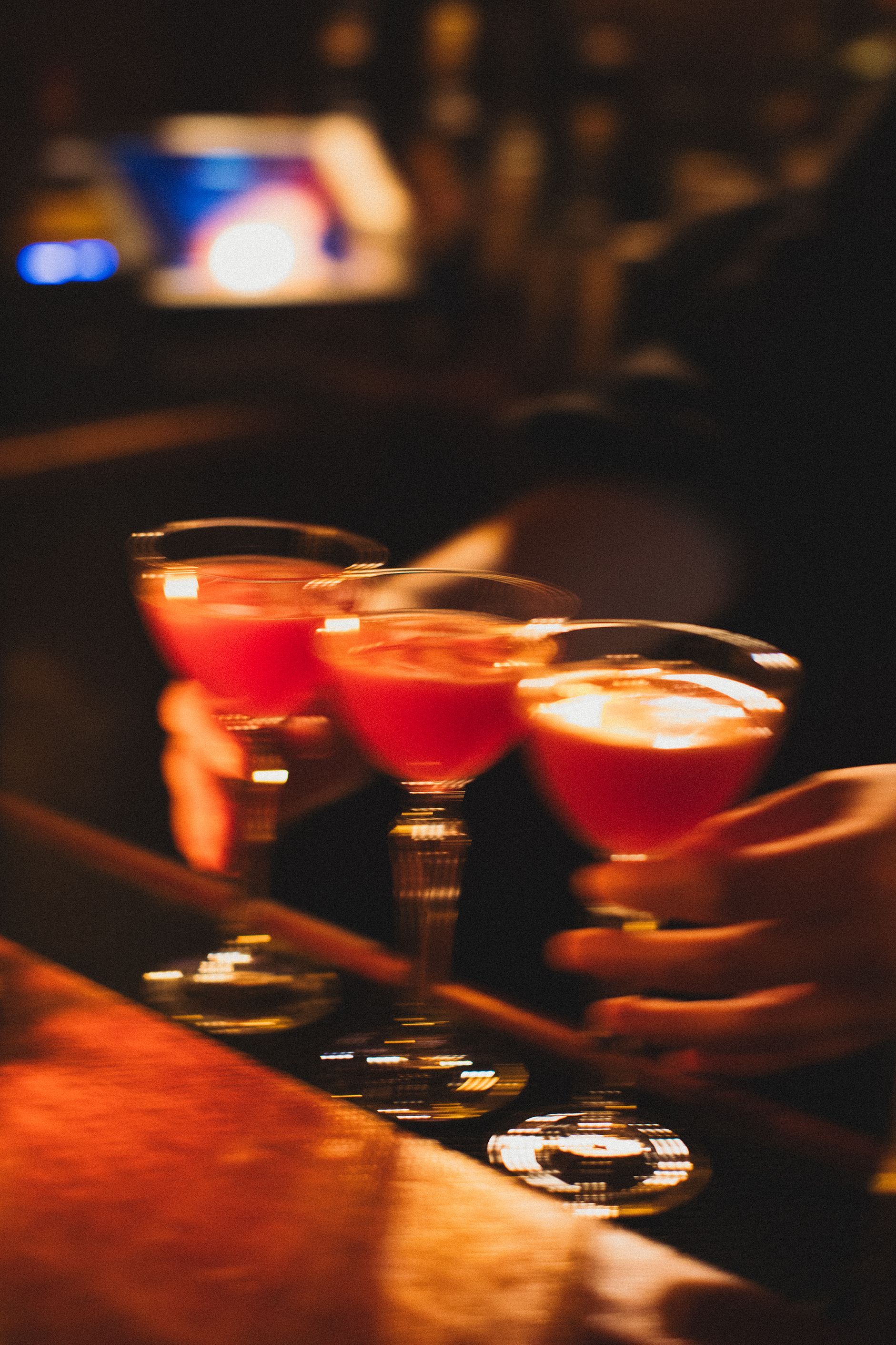 A person is holding three martini glasses with red liquid in them