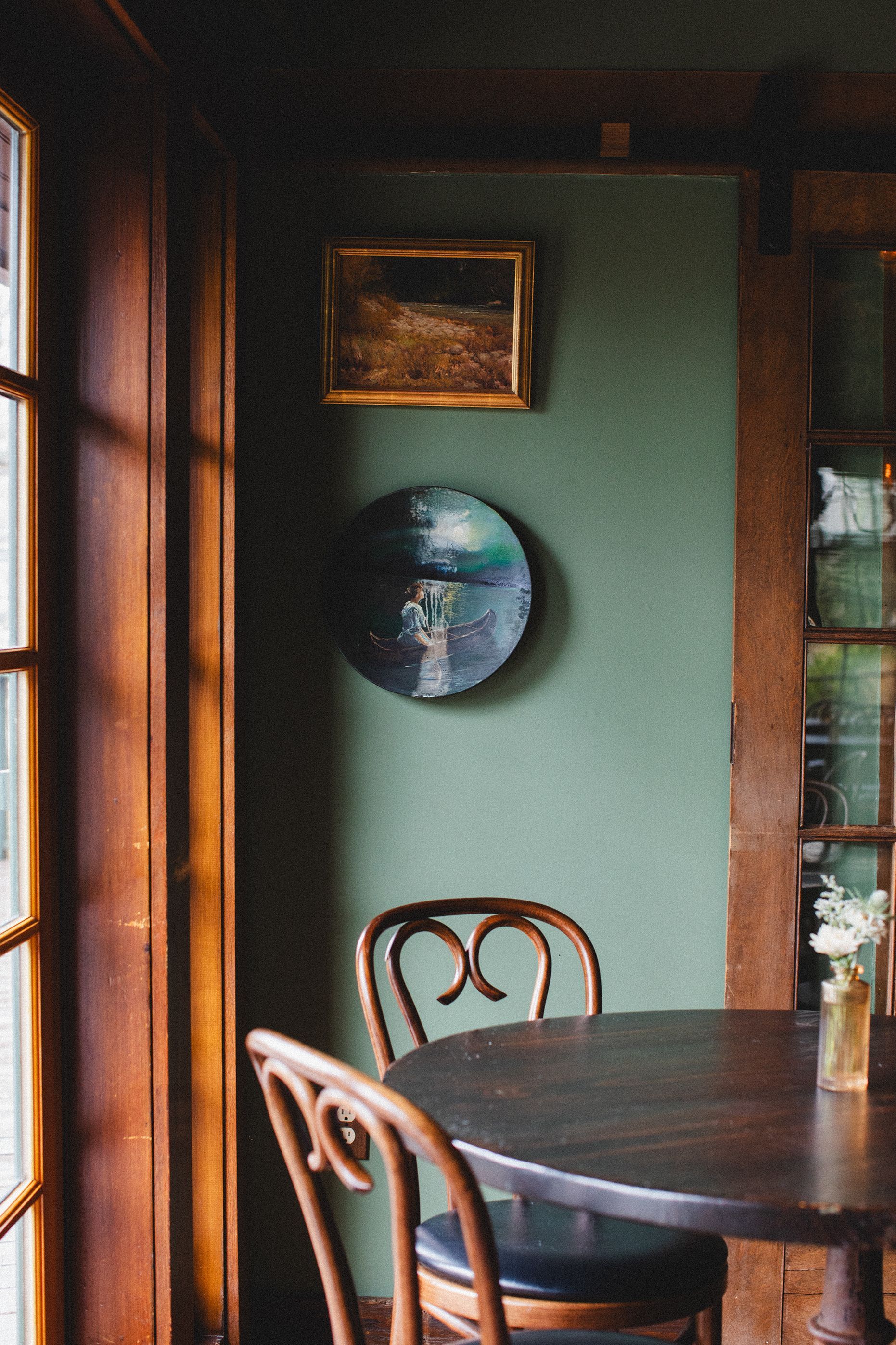 A dining room with a table and chairs and a painting on the wall.