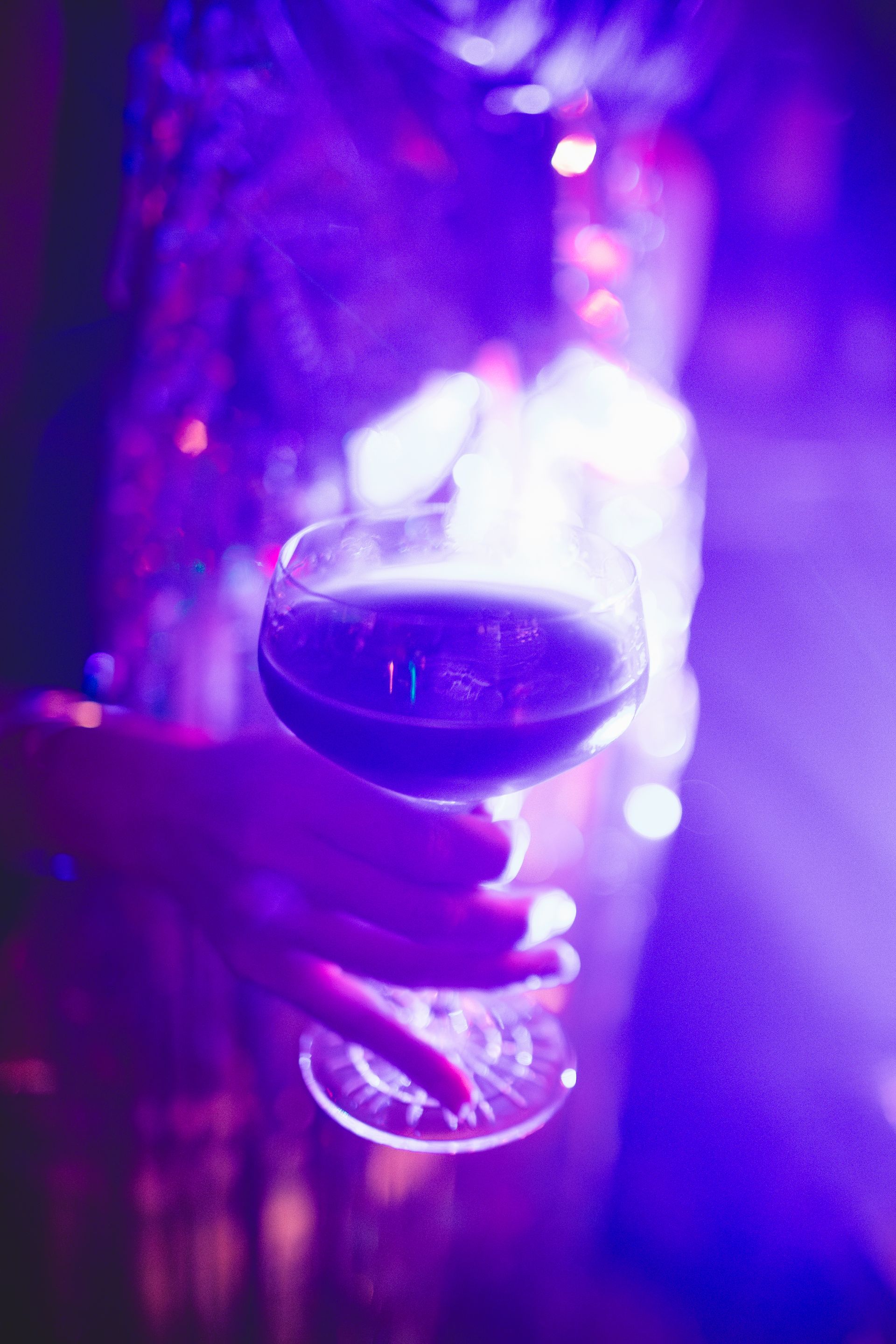 A person is holding a glass of wine in front of a purple background.