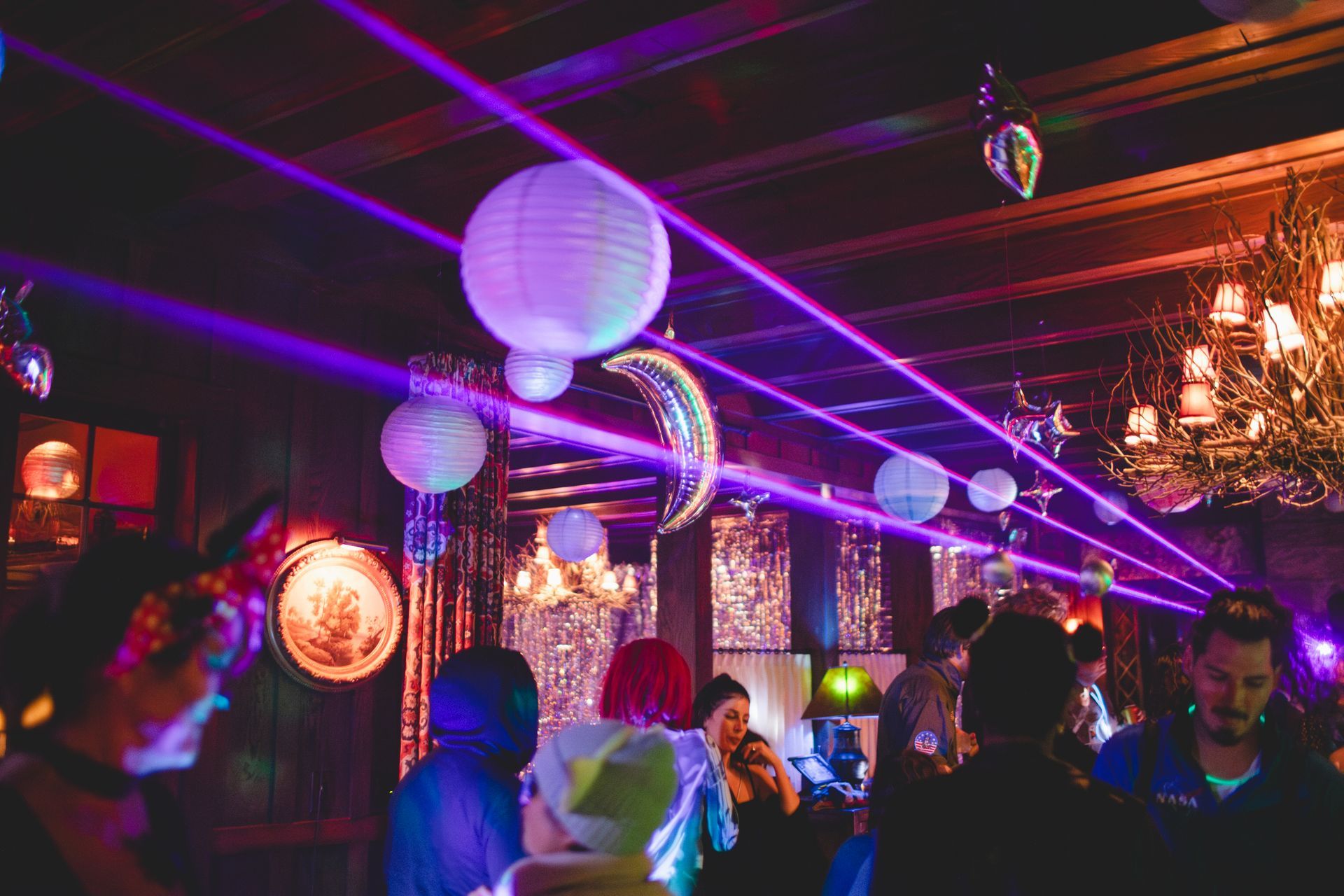 A group of people are dancing in a room with purple lights and balloons hanging from the ceiling.