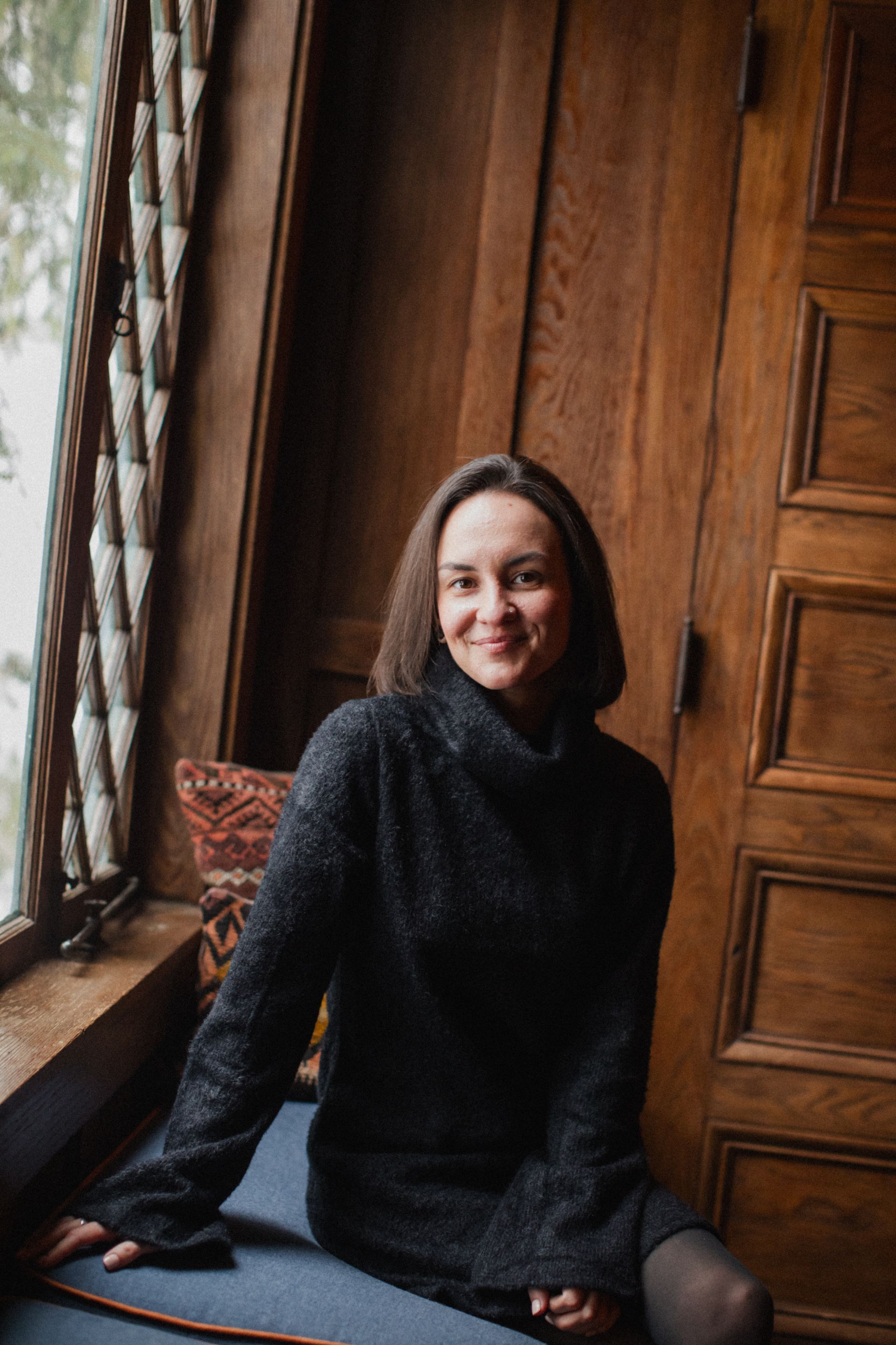 A woman in a black sweater is sitting on a window sill.