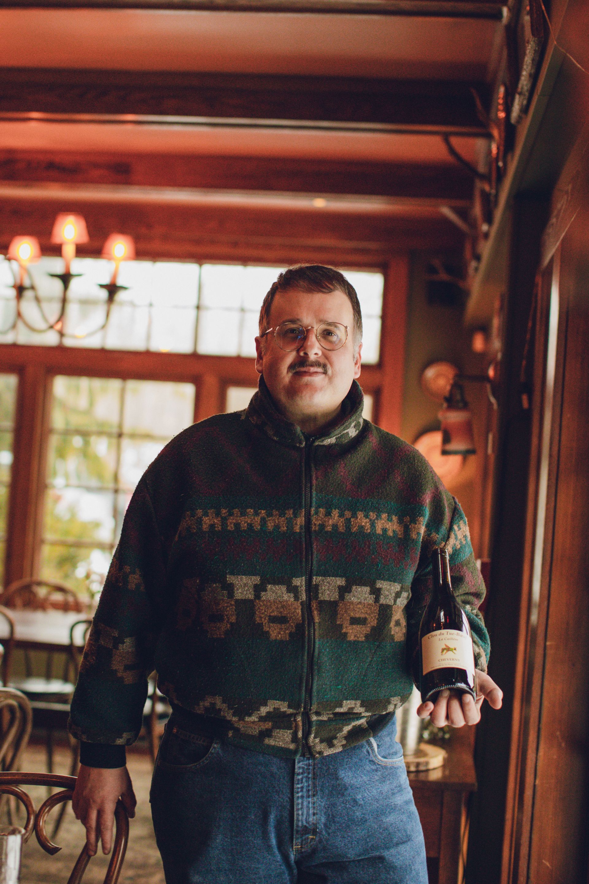 A man in a sweater is holding a bottle of wine