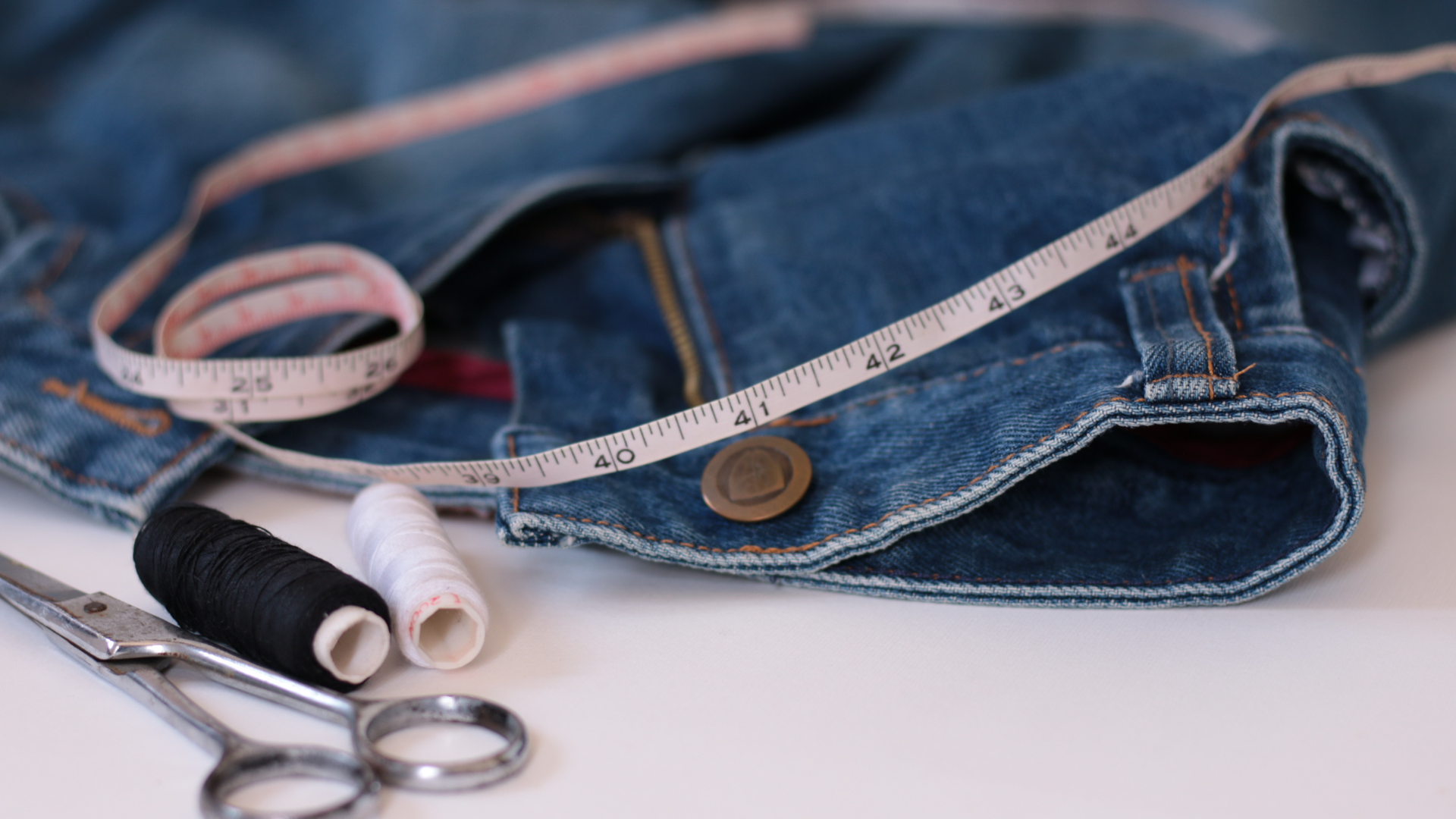 A pair of jeans with a measuring tape , scissors , and spools of thread.