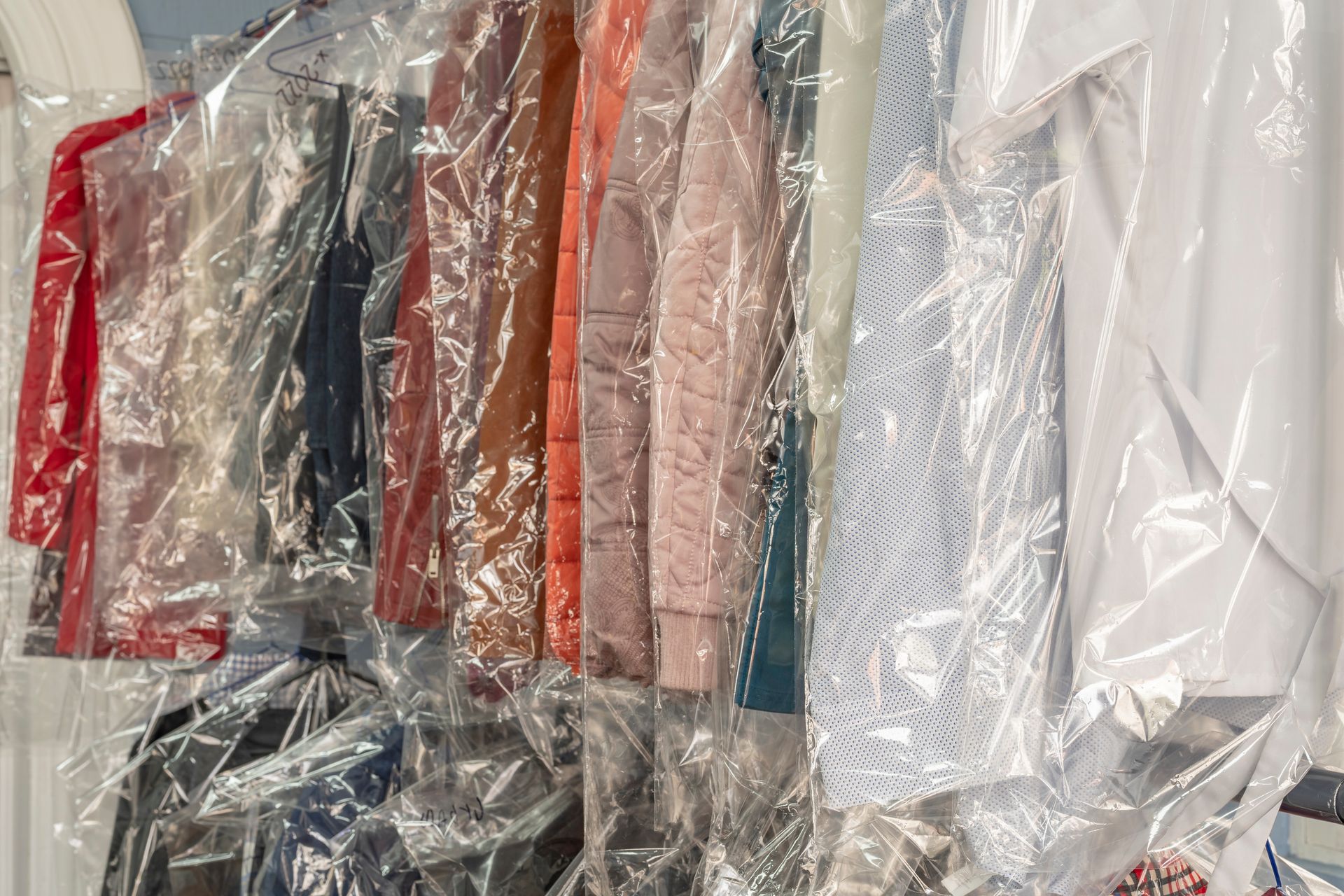 A row of plastic bags filled with clothes hanging on a rack.