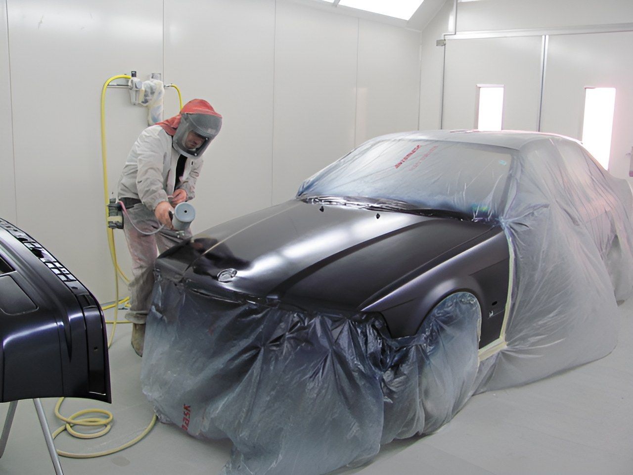 A Man is Painting a Black Car in a Paint Booth — C & C Panel & Paint Mackay In Mackay, QLD