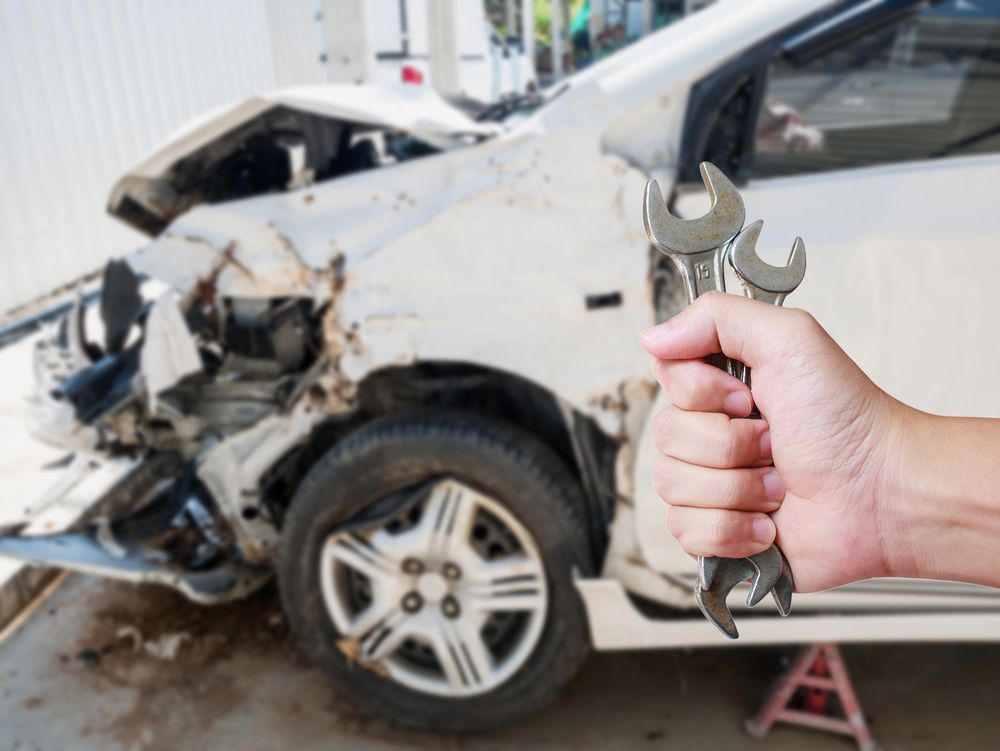 A Person is Holding a Wrench in Front of a Damaged Car — C & C Panel & Paint Mackay In Mackay, QLD