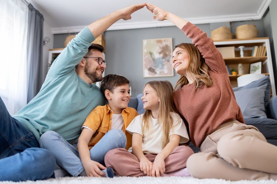 Family sitting on floor, hands forming a roof over their heads.